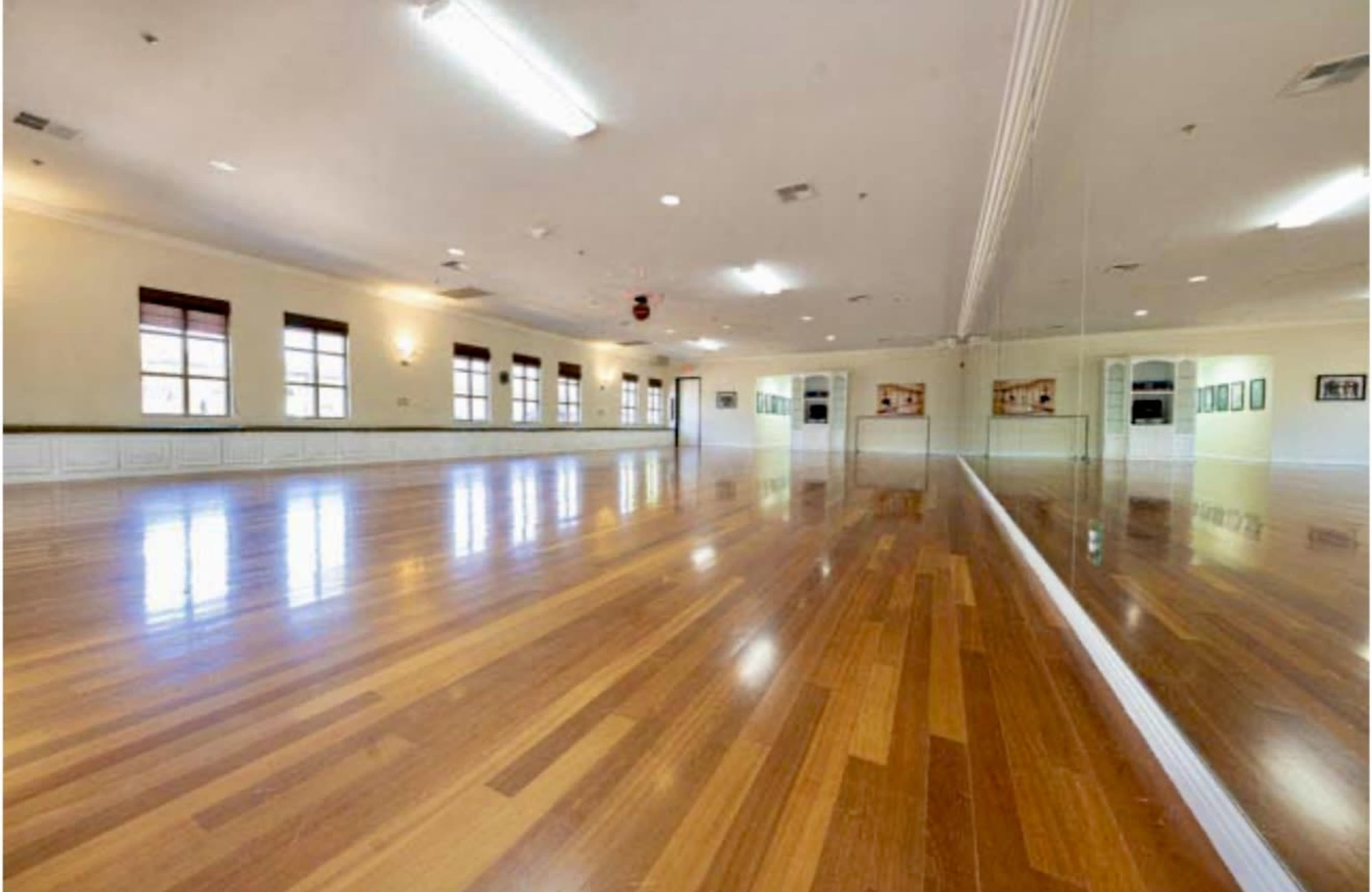 The image shows a spacious, well-lit dance studio with hardwood floors and large mirrors along one wall.