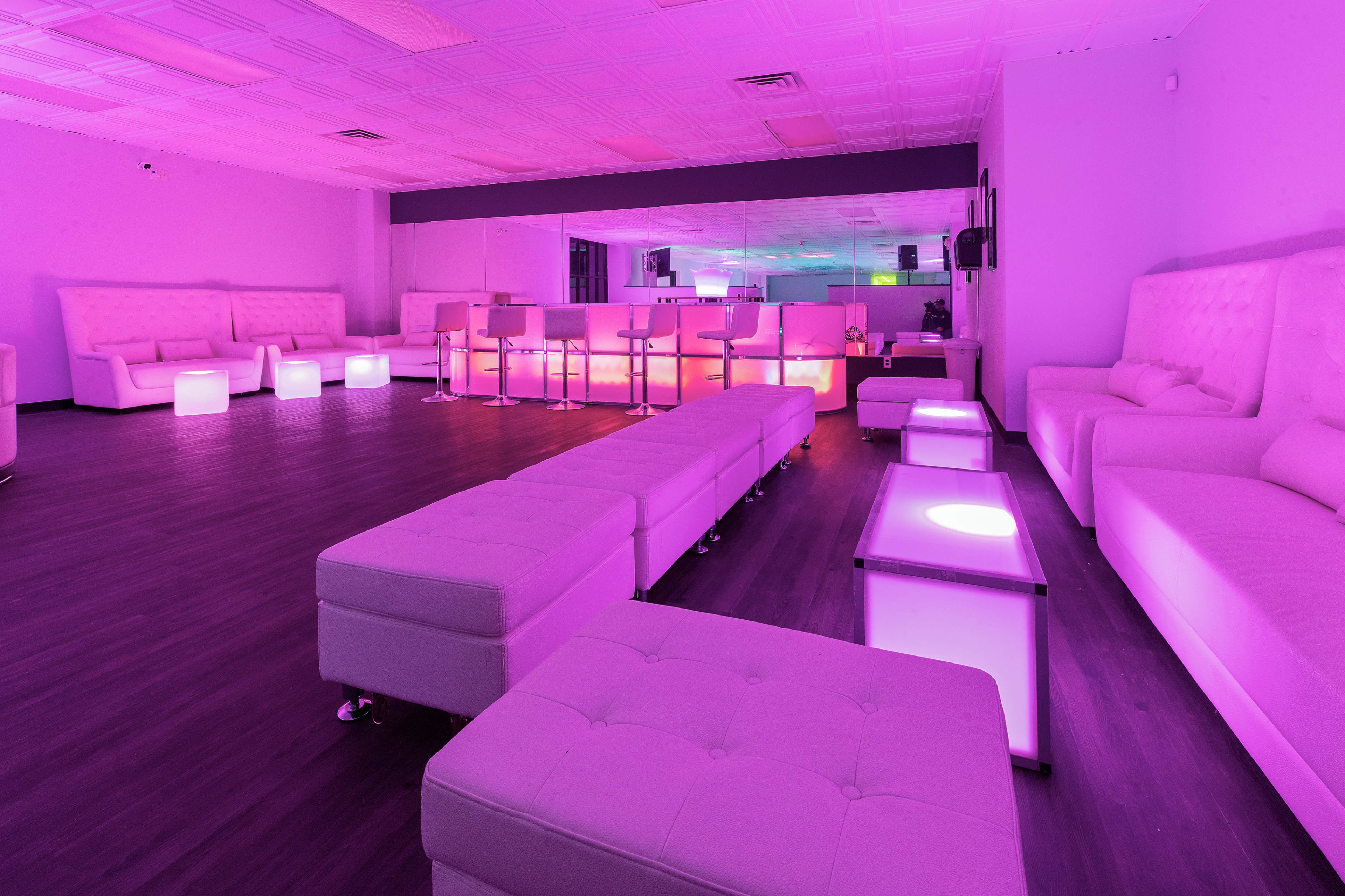 The image shows a modern lounge area with white furniture and dim, colorful lighting.