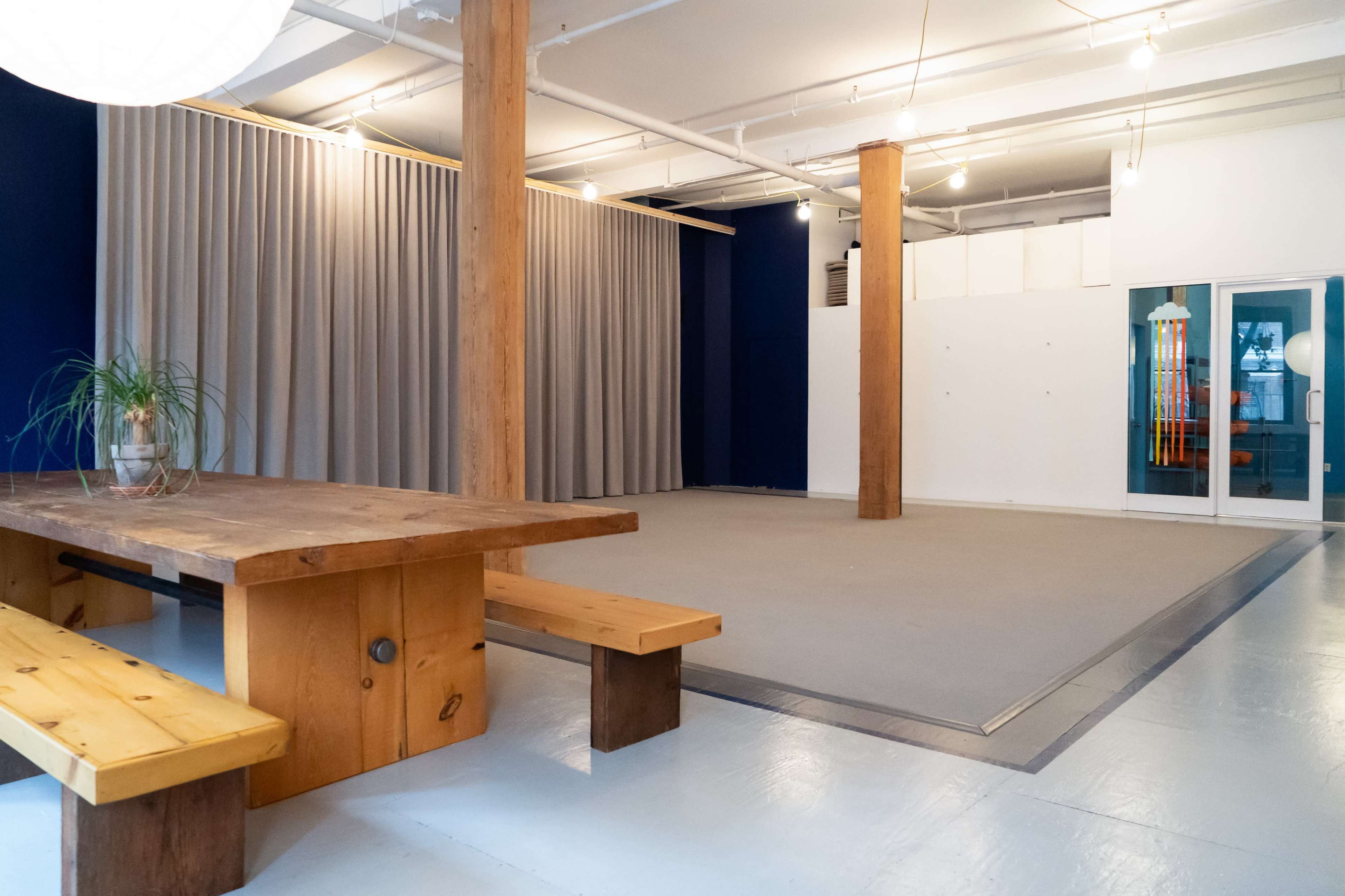 The image shows a spacious interior with wooden benches, a large table, and a curtain-covered area against a blue wall.