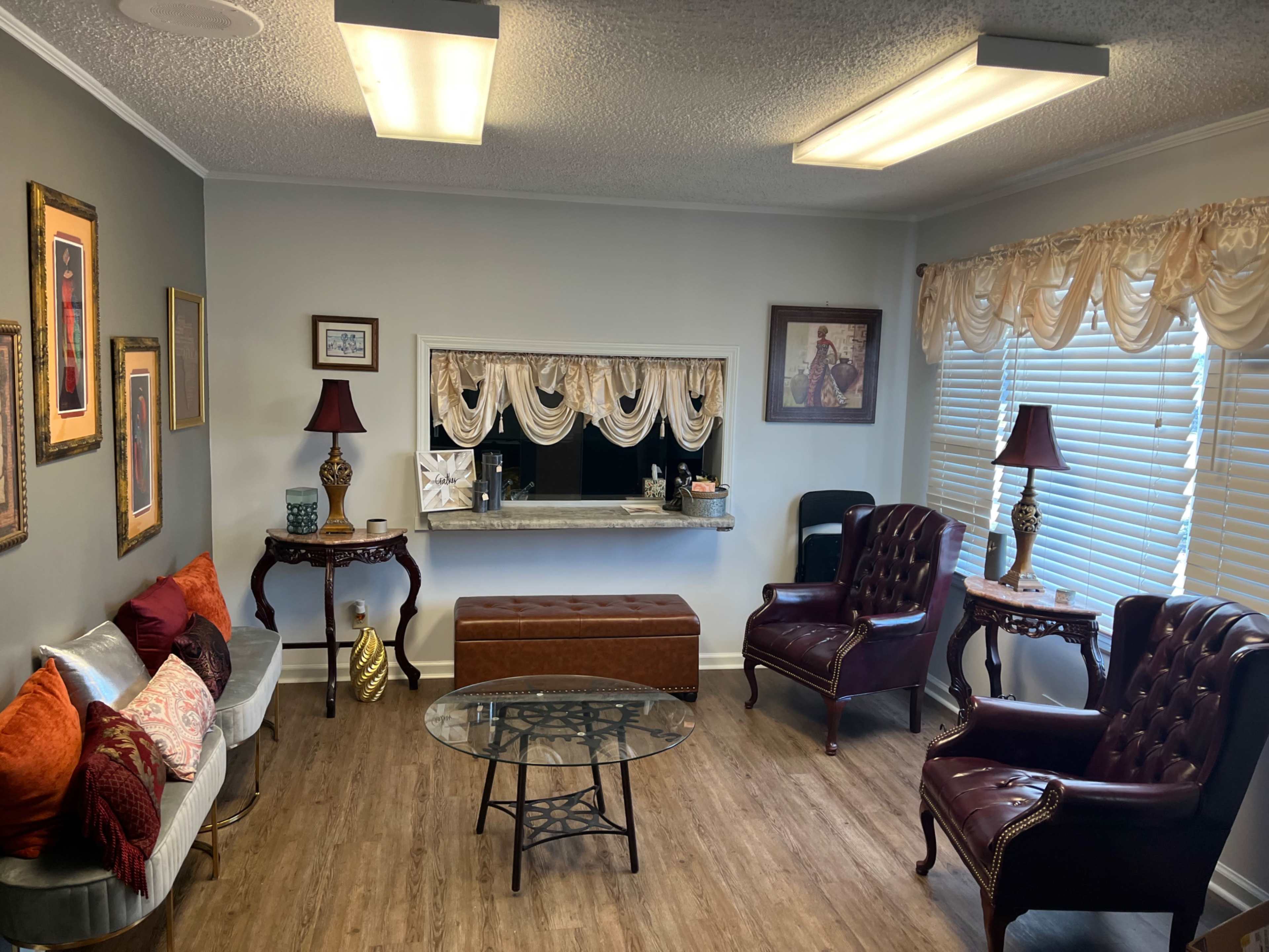 The image shows a cozy waiting room with two plush armchairs, a coffee table, and decorative wall art.