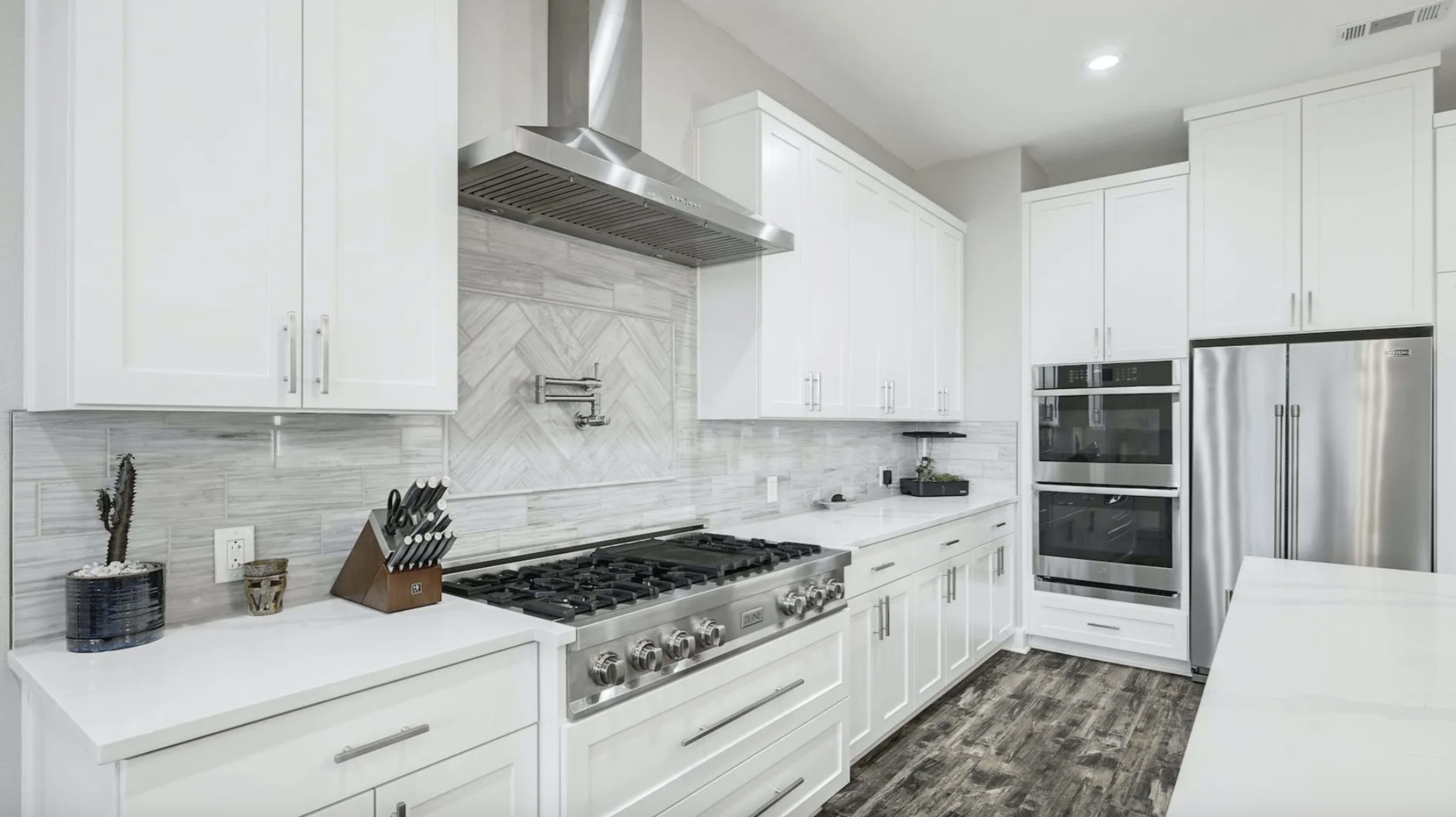 The image shows a modern kitchen with white cabinetry, a large stainless steel gas stove, and a sleek combination of a built-in oven and microwave.