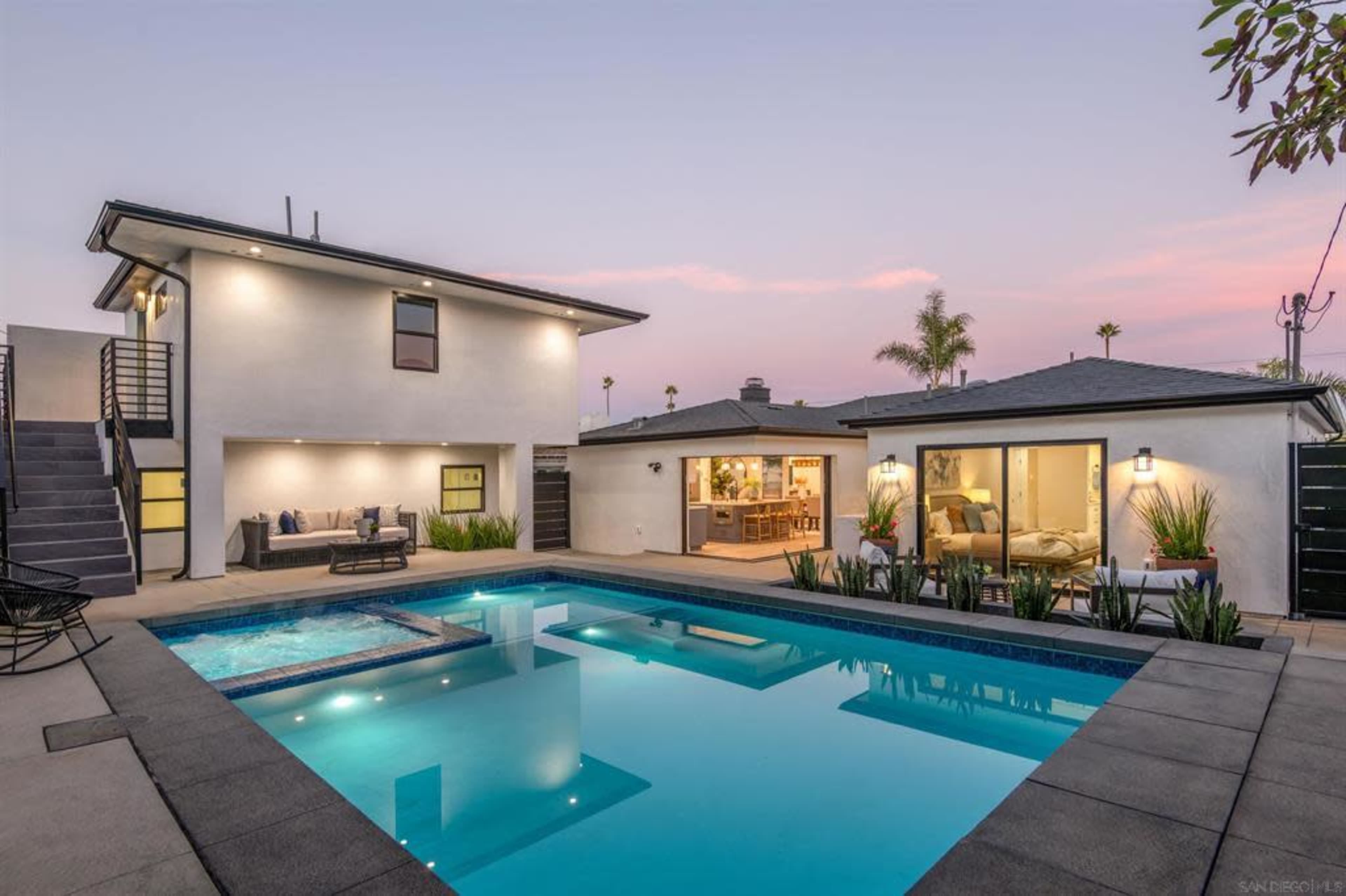 A modern two-story home with a pool and spa is surrounded by landscaped greenery and has a patio area for outdoor relaxation.