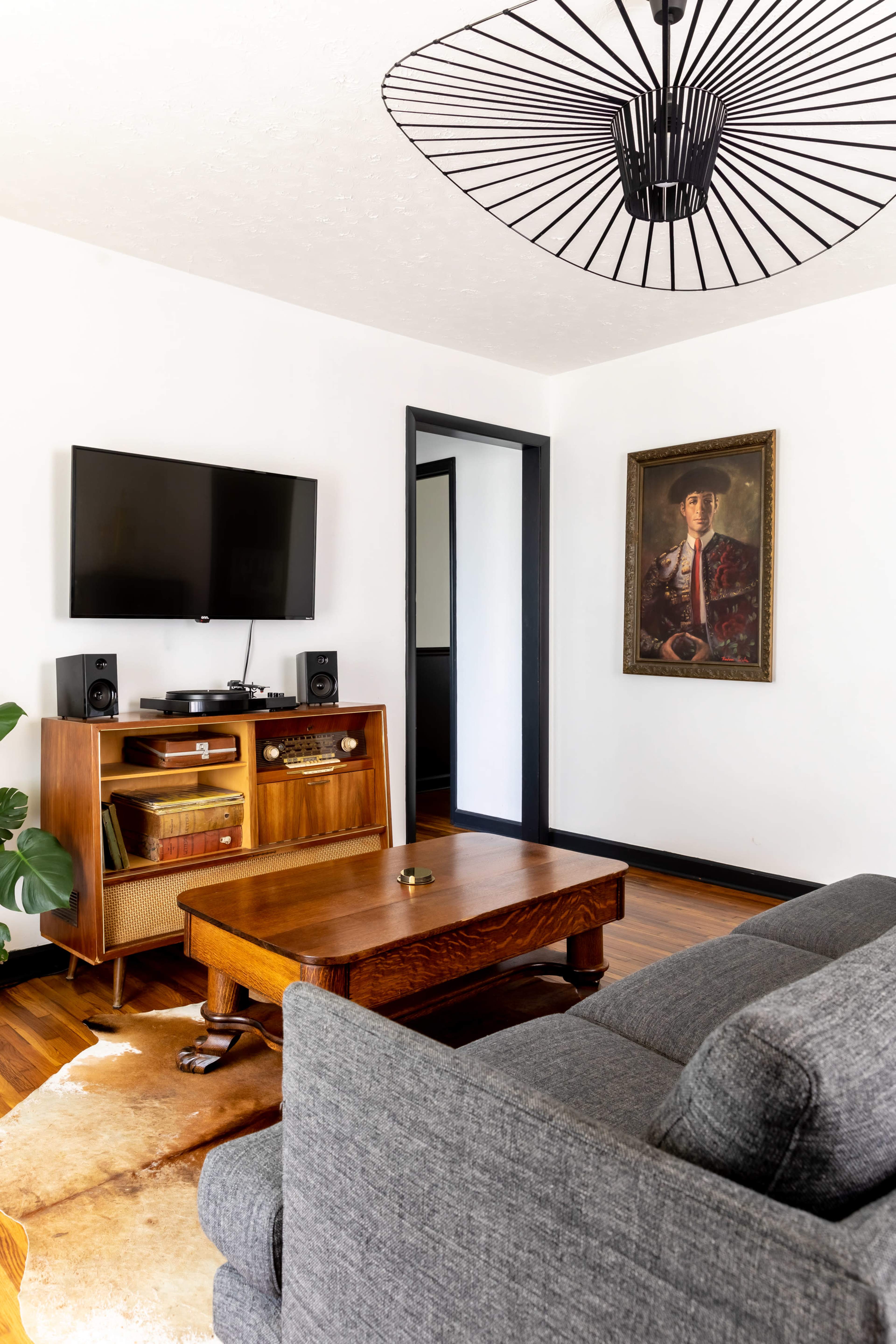 A living room with a gray sofa, a wooden coffee table, a media console under a wall-mounted TV, and a framed portrait on the wall.