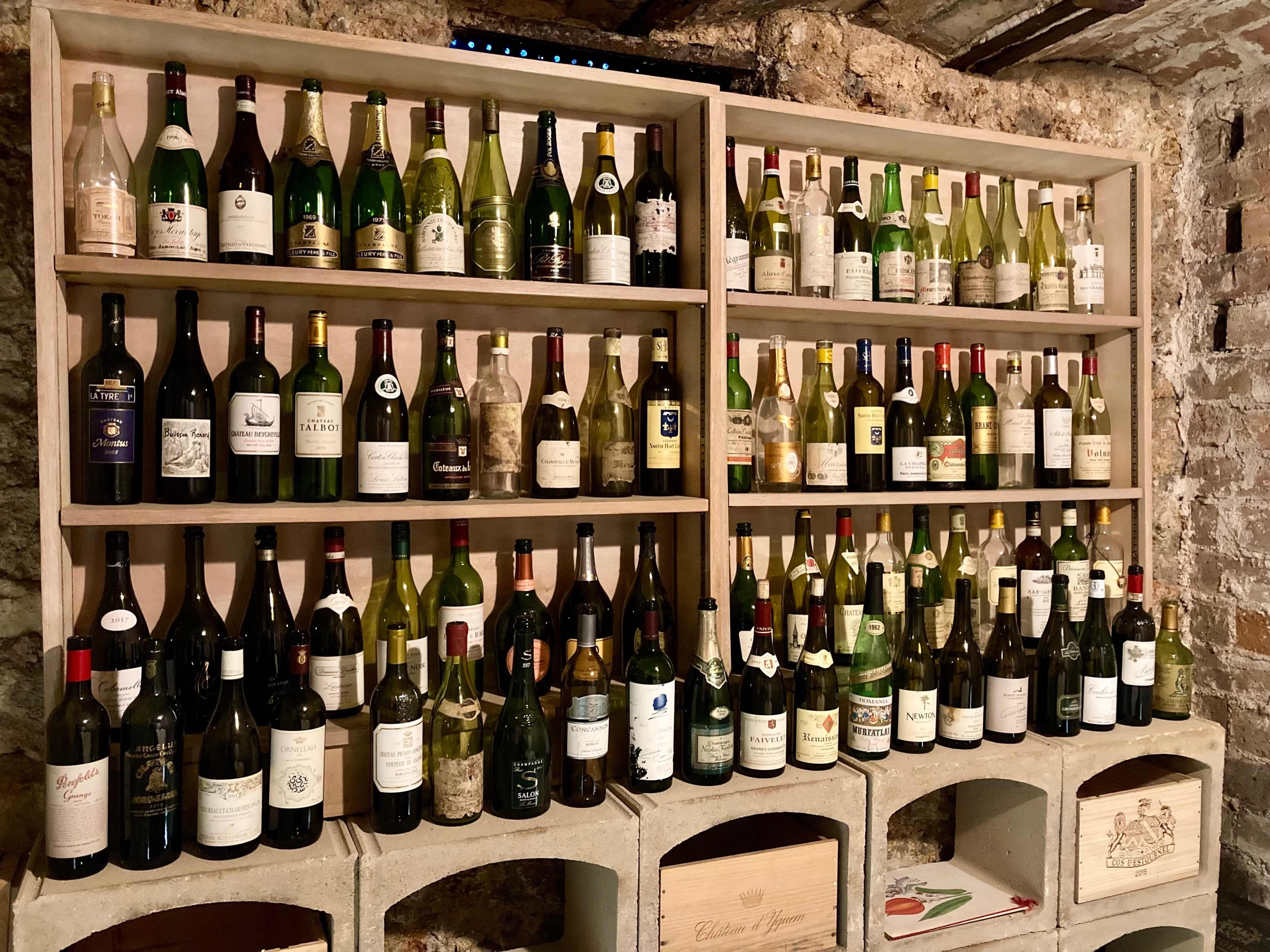 A wooden shelf holds various bottles of wine arranged neatly against a brick wall.