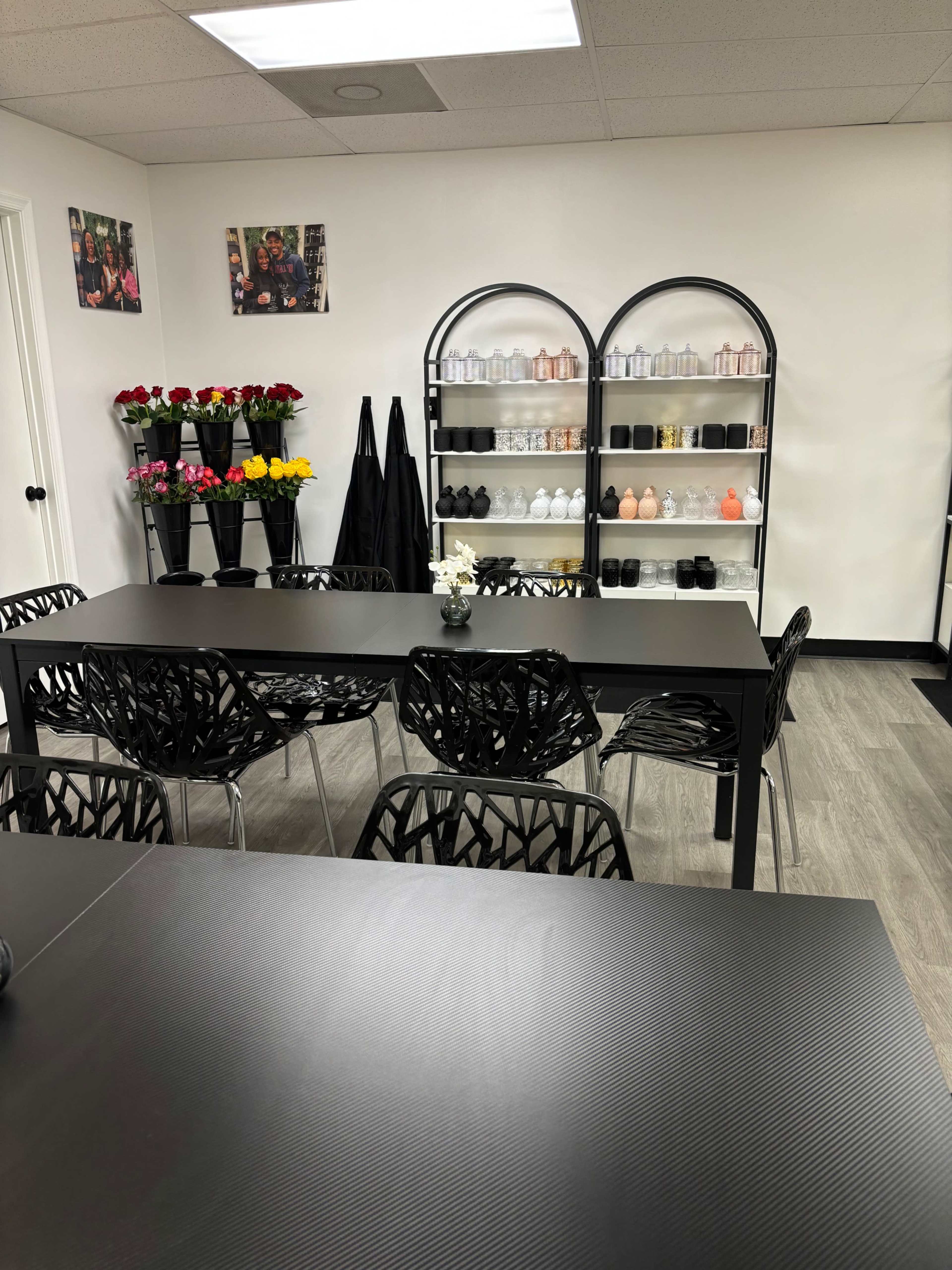 A modern interior of a room with black tables and chairs, flower arrangements, and a shelving unit displaying various bottles.