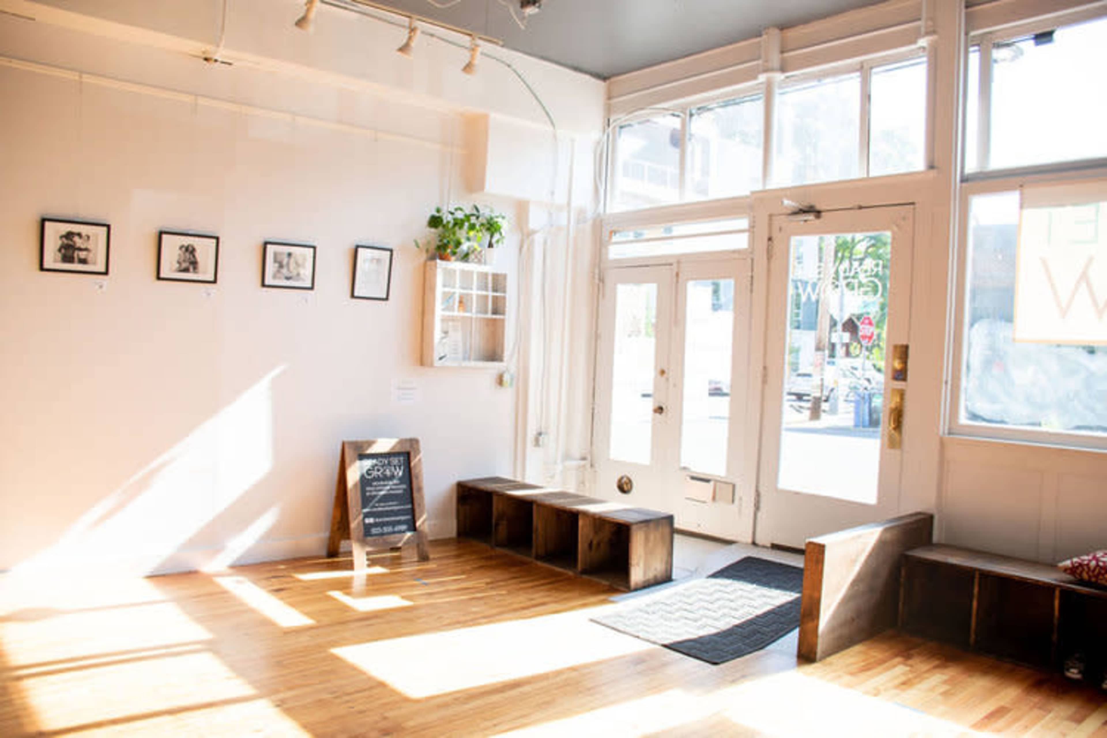 A bright, minimalist interior with wooden flooring, a few framed pictures on the walls, and a bench near the entrance.