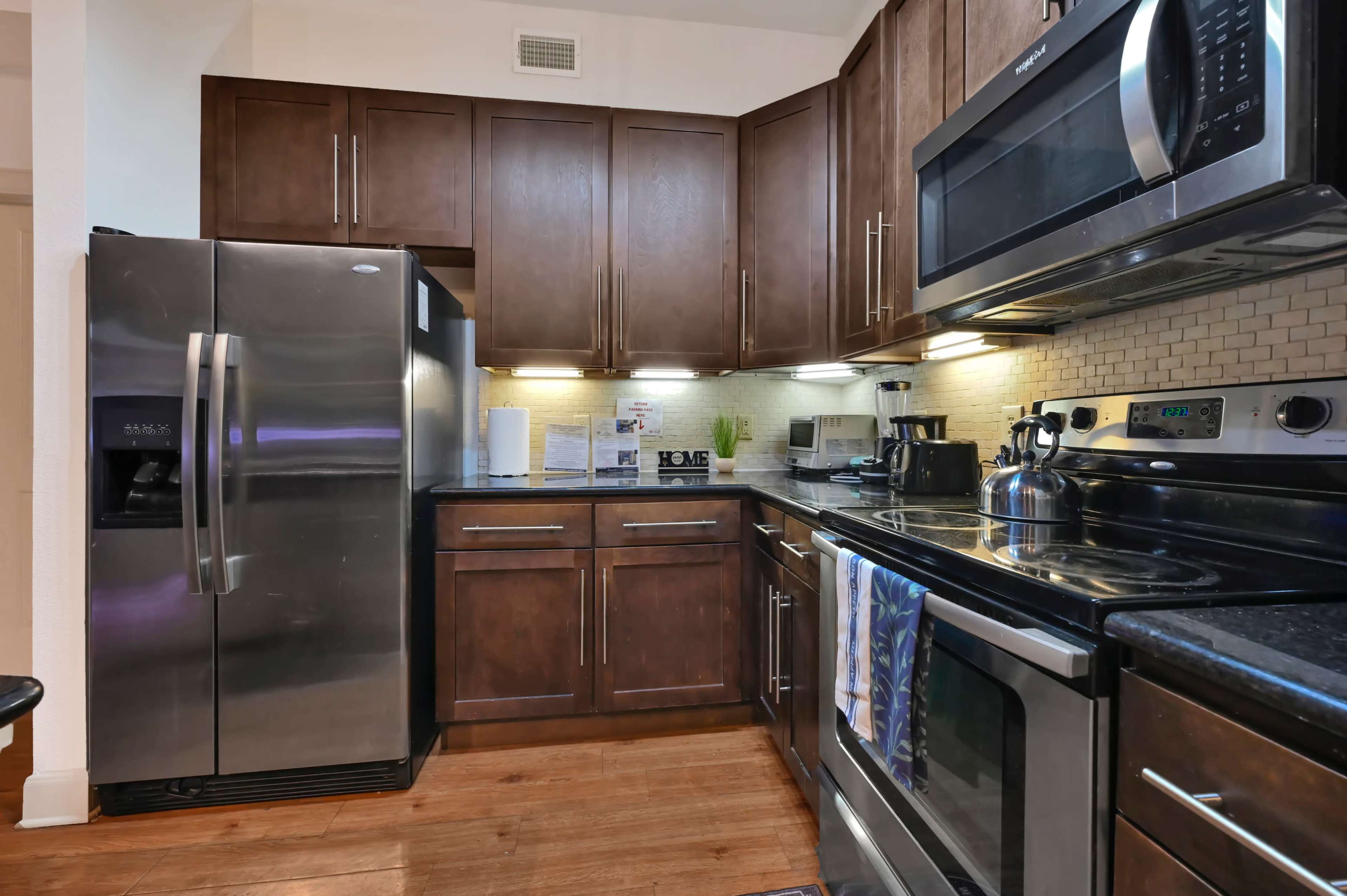 The image shows a modern kitchen with dark wood cabinets, stainless steel appliances, and a black countertop.