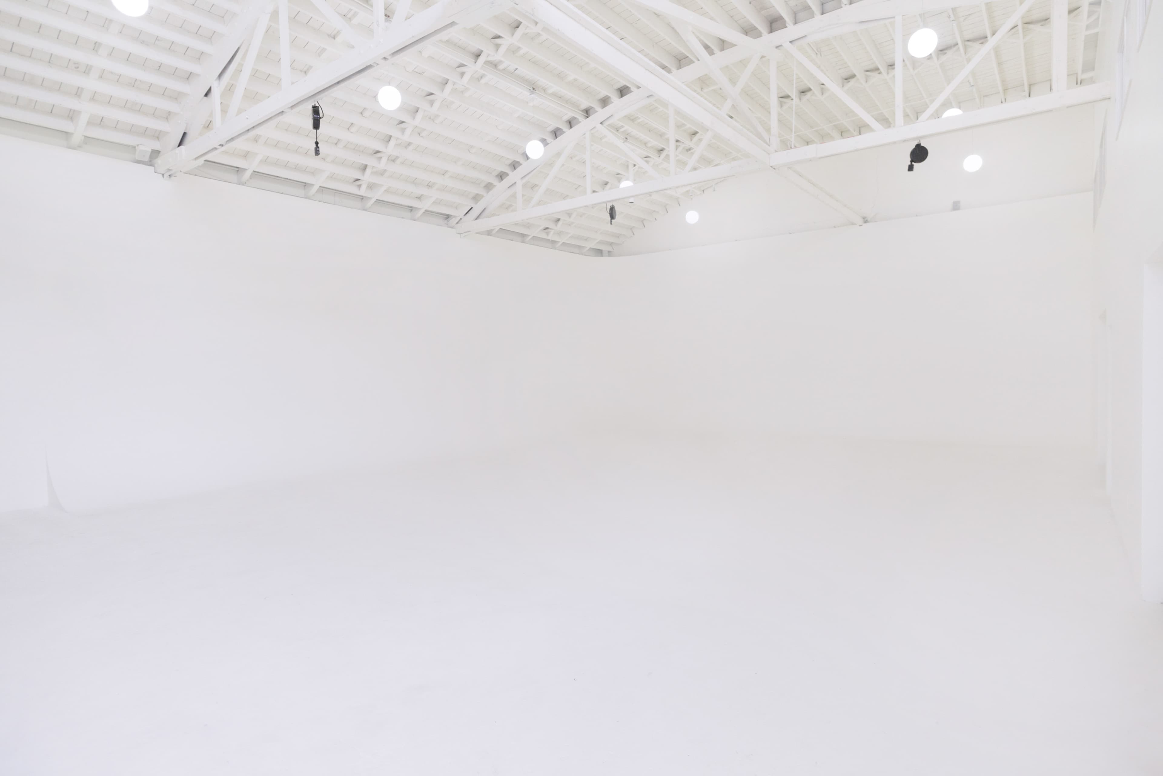 A spacious, empty room with white walls and a white ceiling, illuminated by ceiling lights.