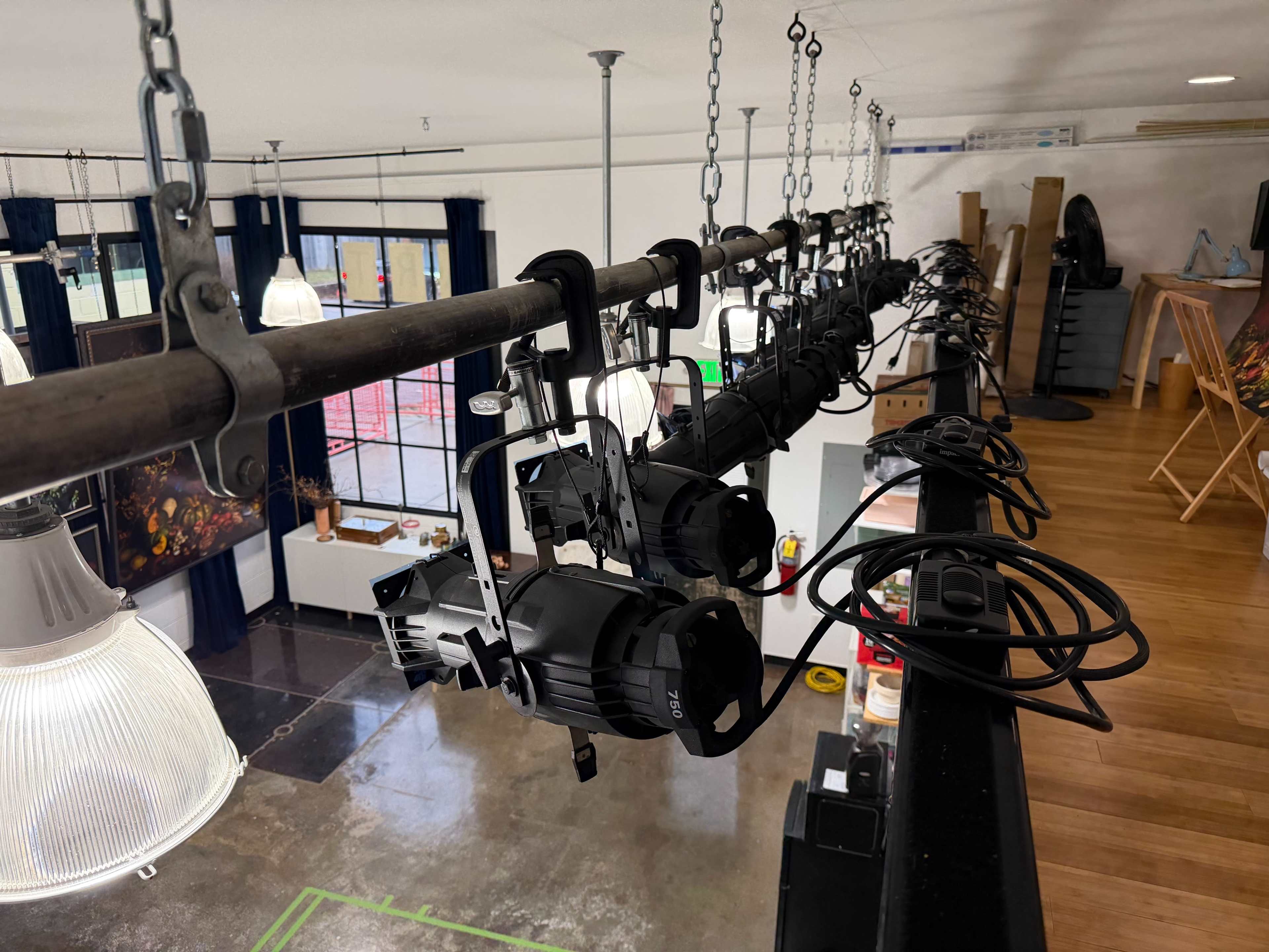 The image shows a row of stage lights suspended from a beam in a well-lit interior space.