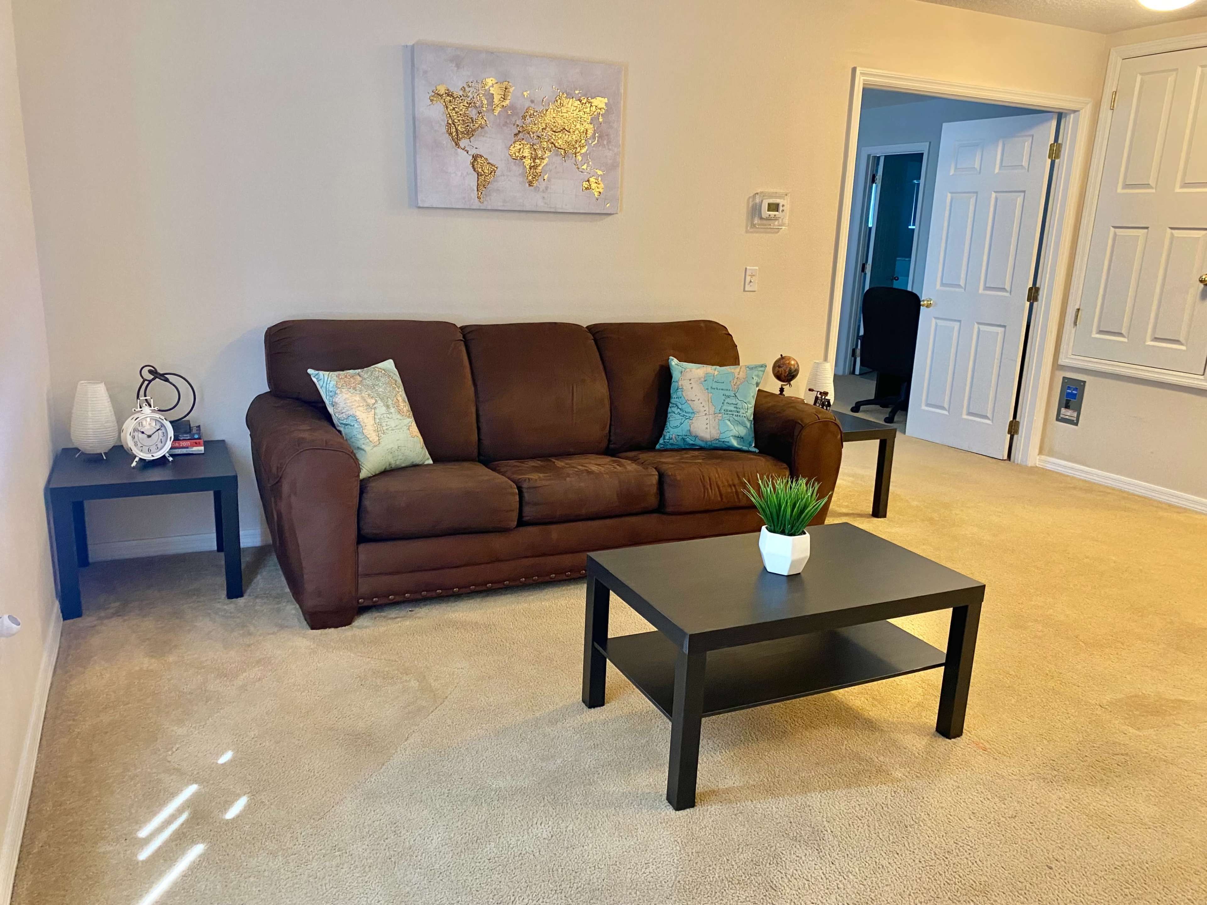 A living room with a brown sofa, a coffee table, and a wall-mounted world map above the couch.