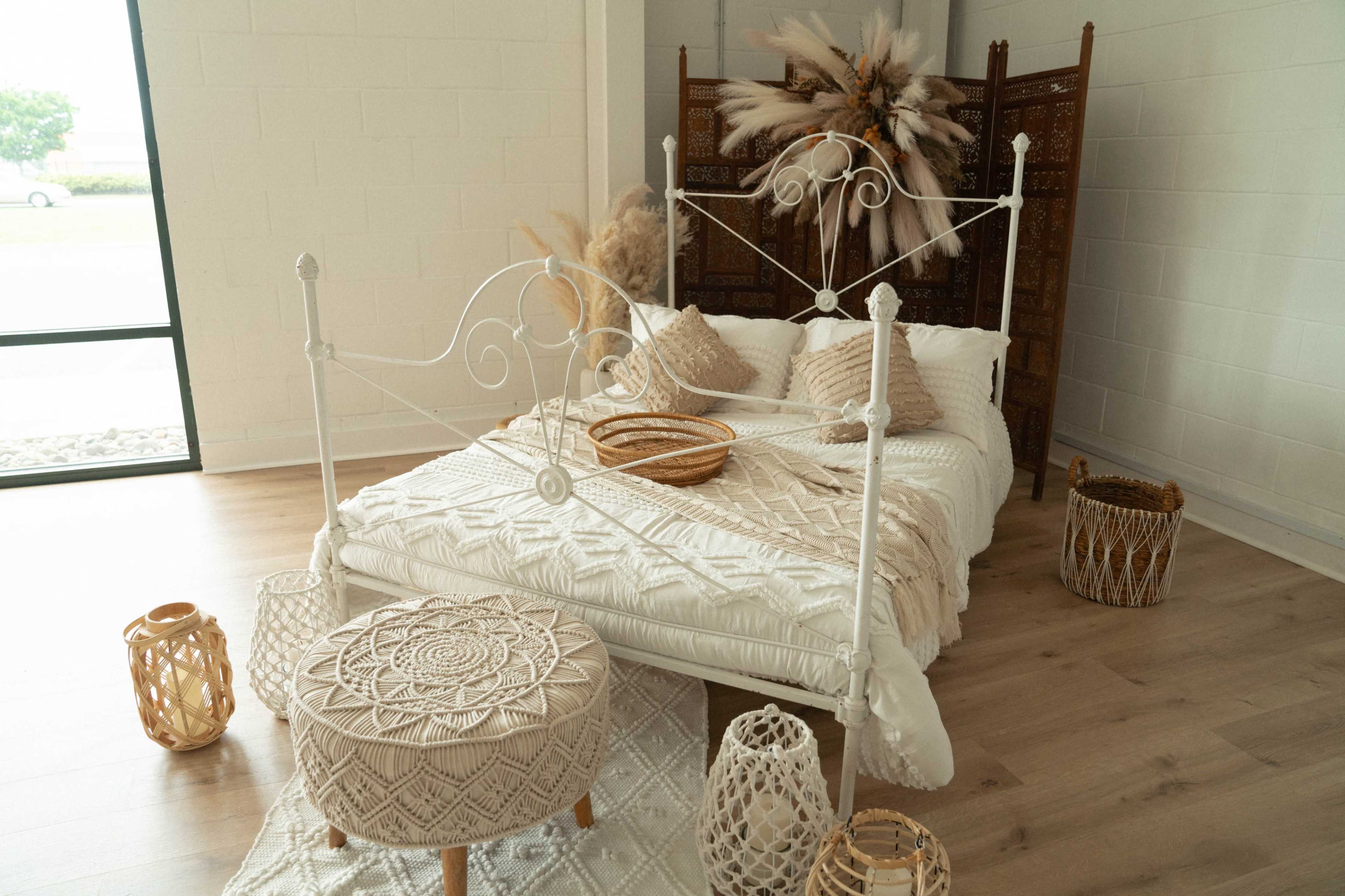 A cozy bedroom featuring a white metal bed adorned with textured blankets and pillows, surrounded by woven baskets and decorative lanterns.