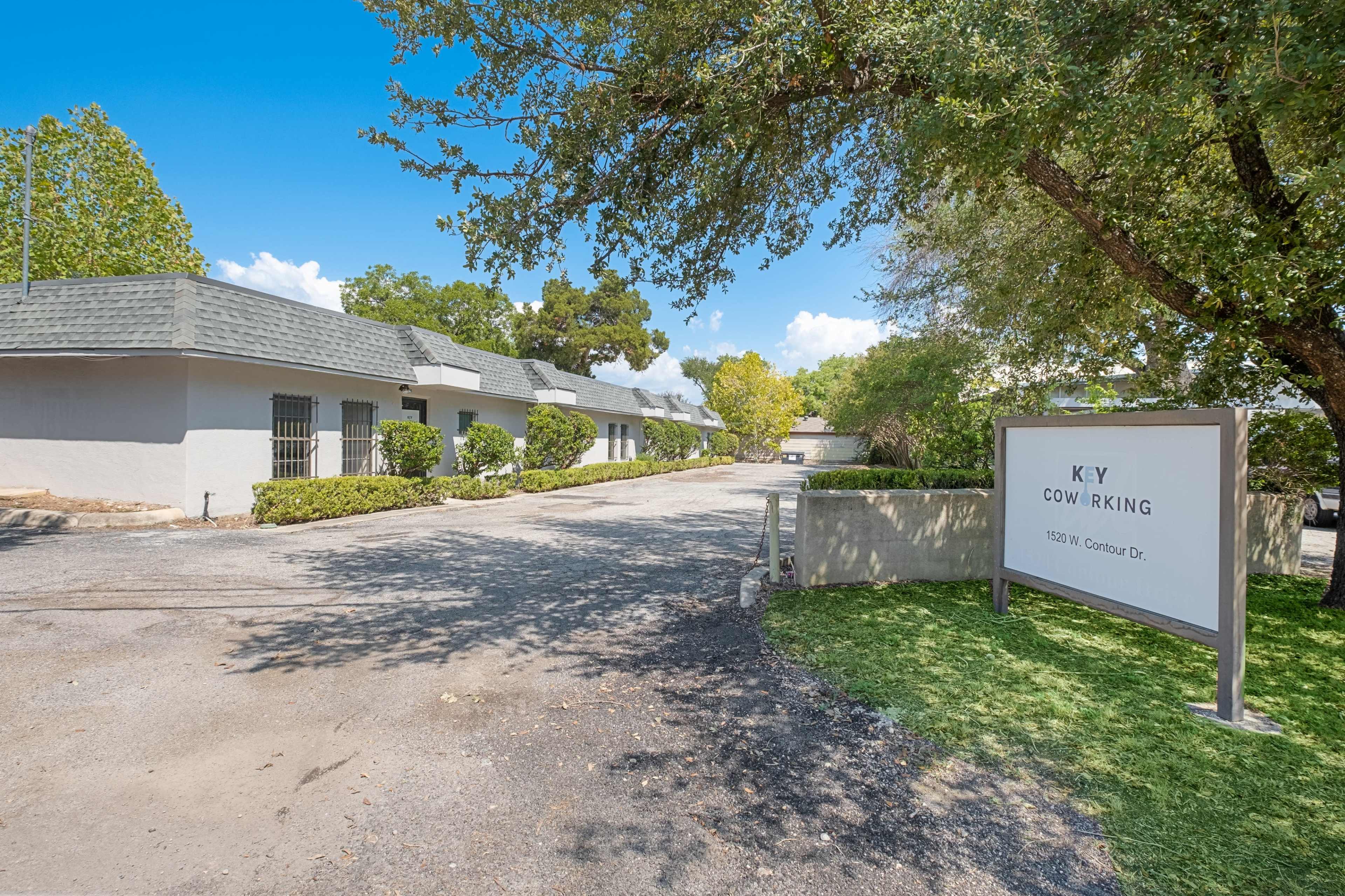 The image shows a co-working space with a sign reading "KY Coworking" near a gravel driveway lined with trees and shrubs.