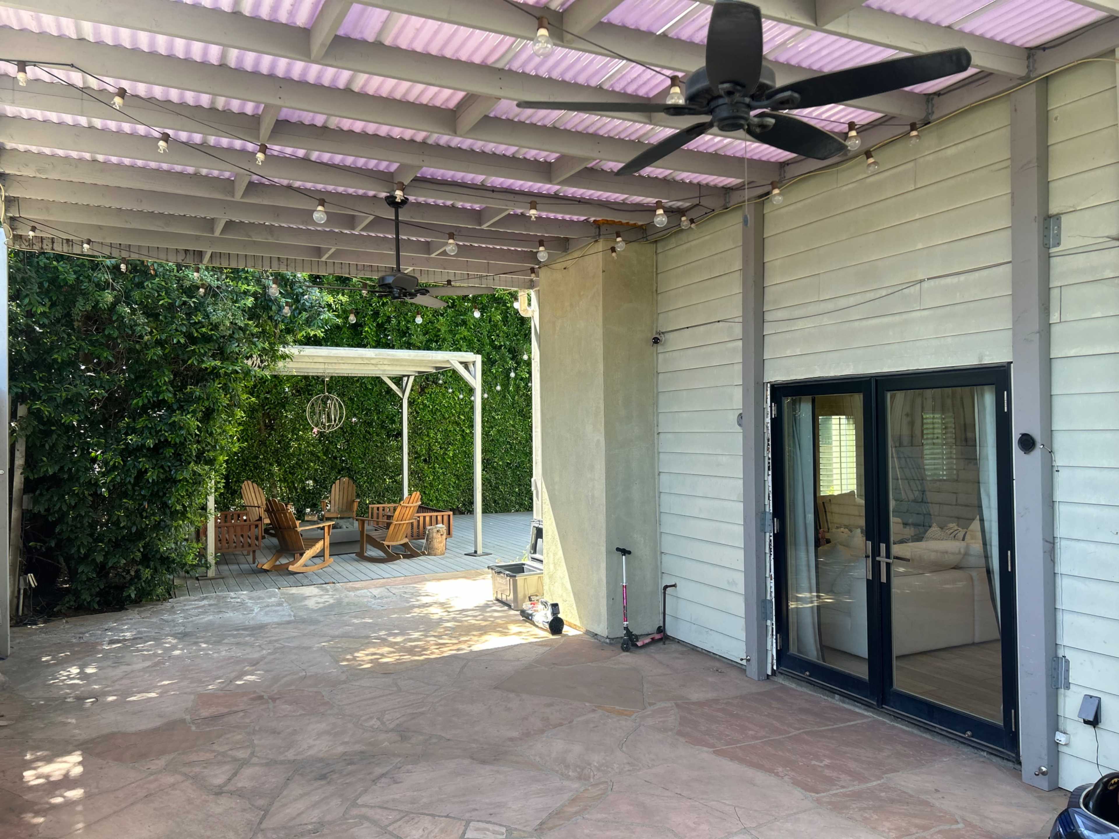 A covered patio area with a stone floor, several ceiling fans, and a view of a seating area surrounded by greenery.