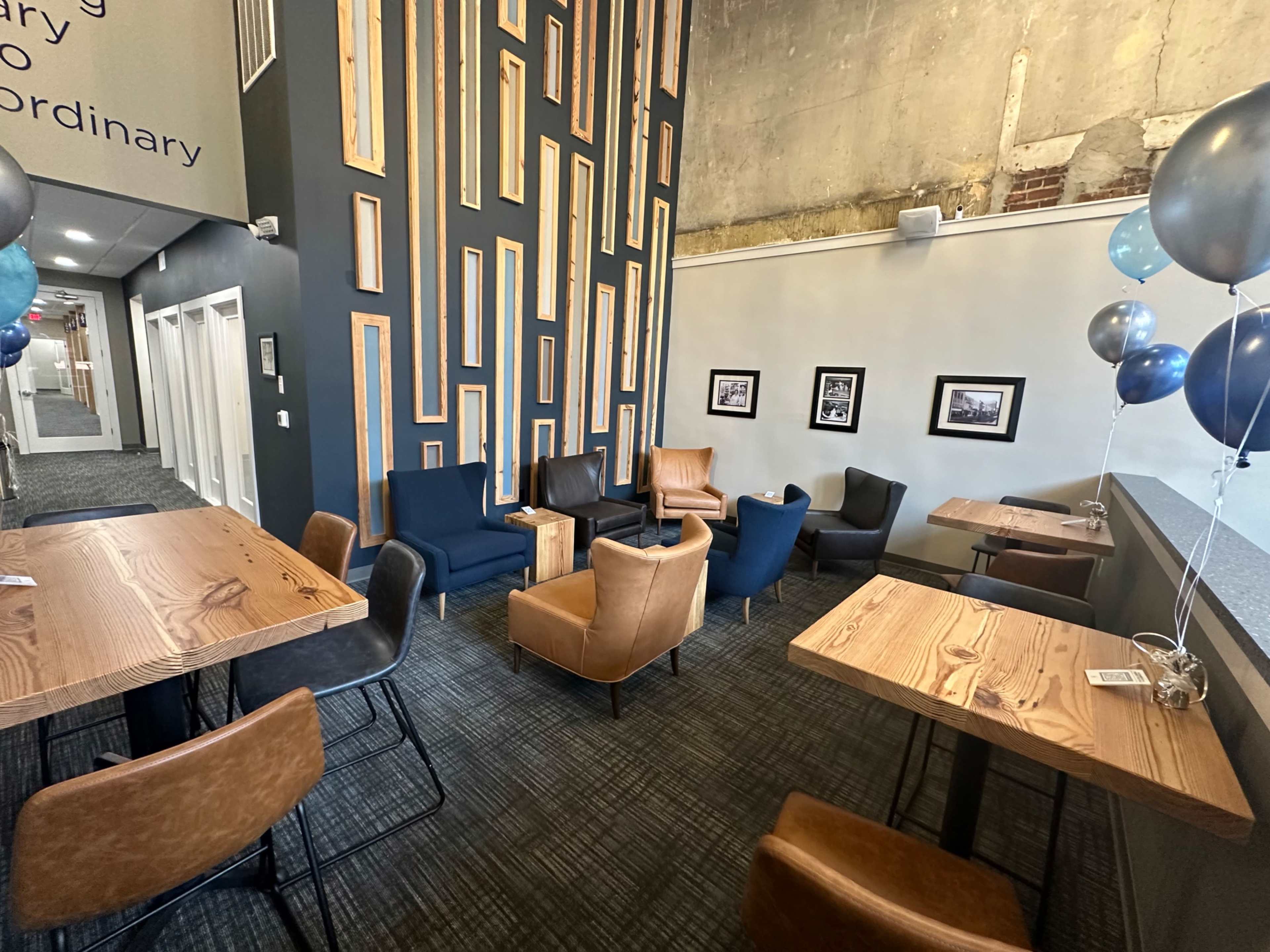 A modern seating area with several chairs around wooden tables, accented by a textured wall and decorative balloons.