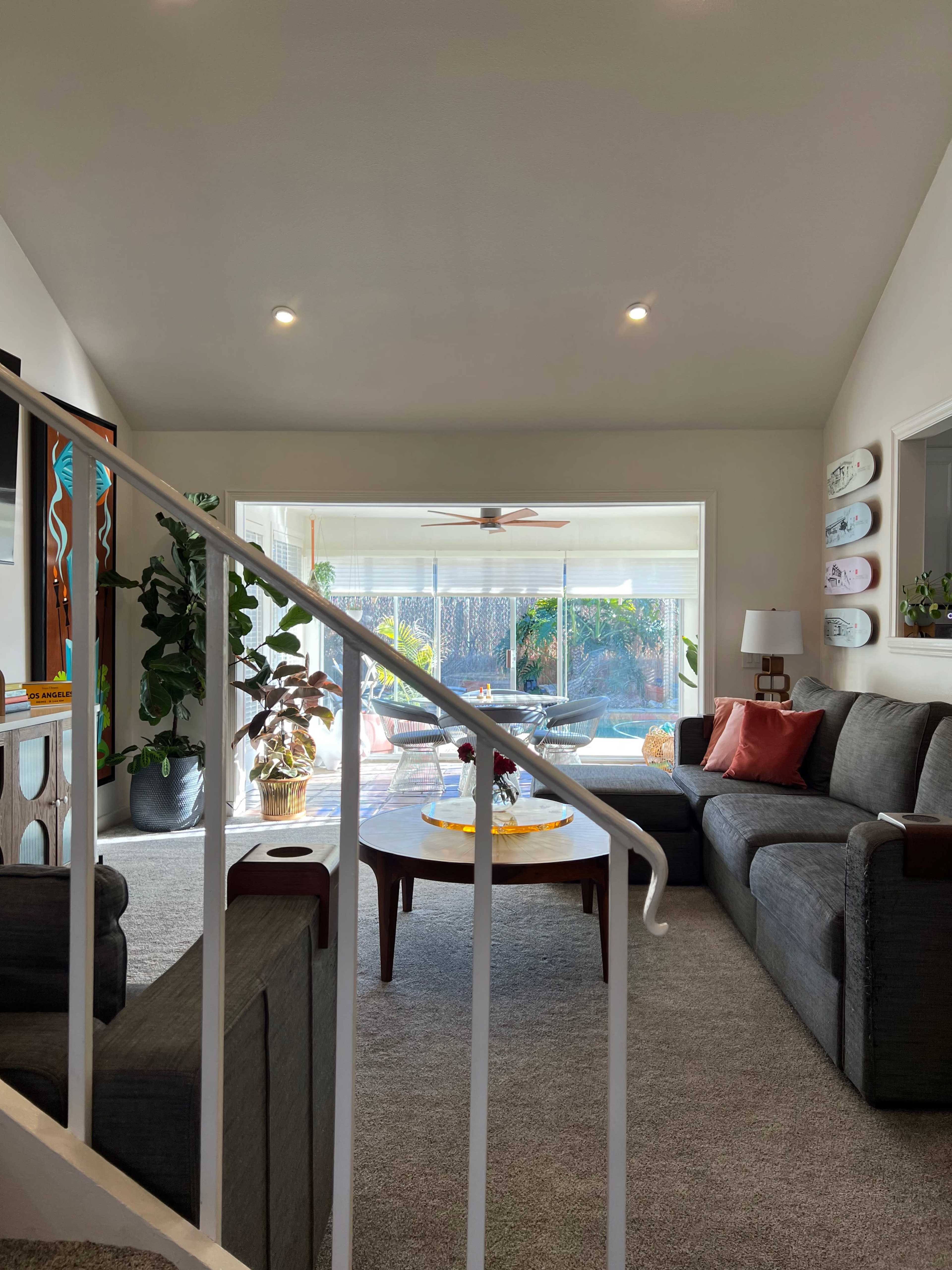 A bright living room features a gray sectional sofa, a round coffee table with snacks, and large windows overlooking a patio area.