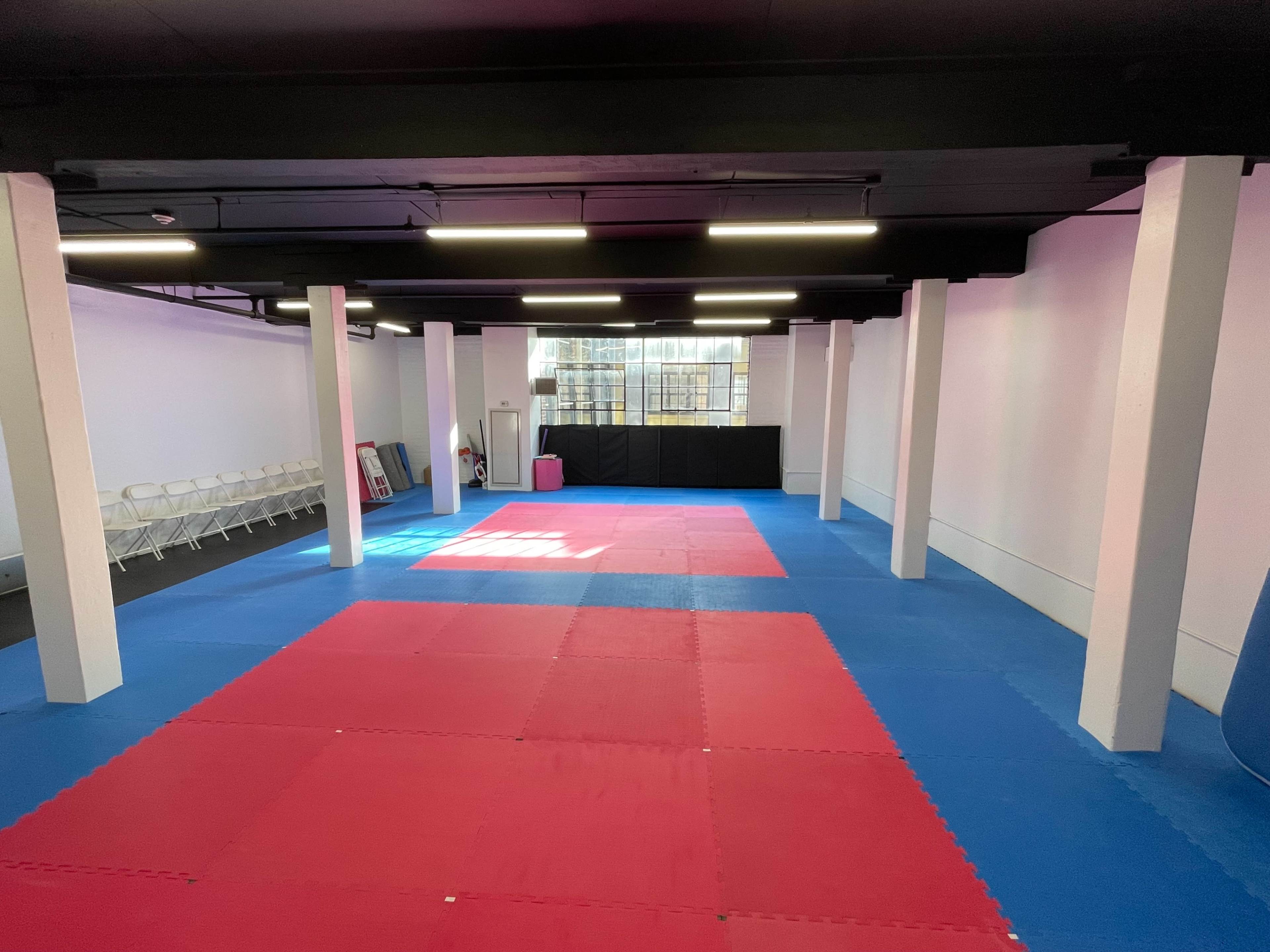 A spacious training room with red and blue mats, white pillars, and a row of chairs along one wall.