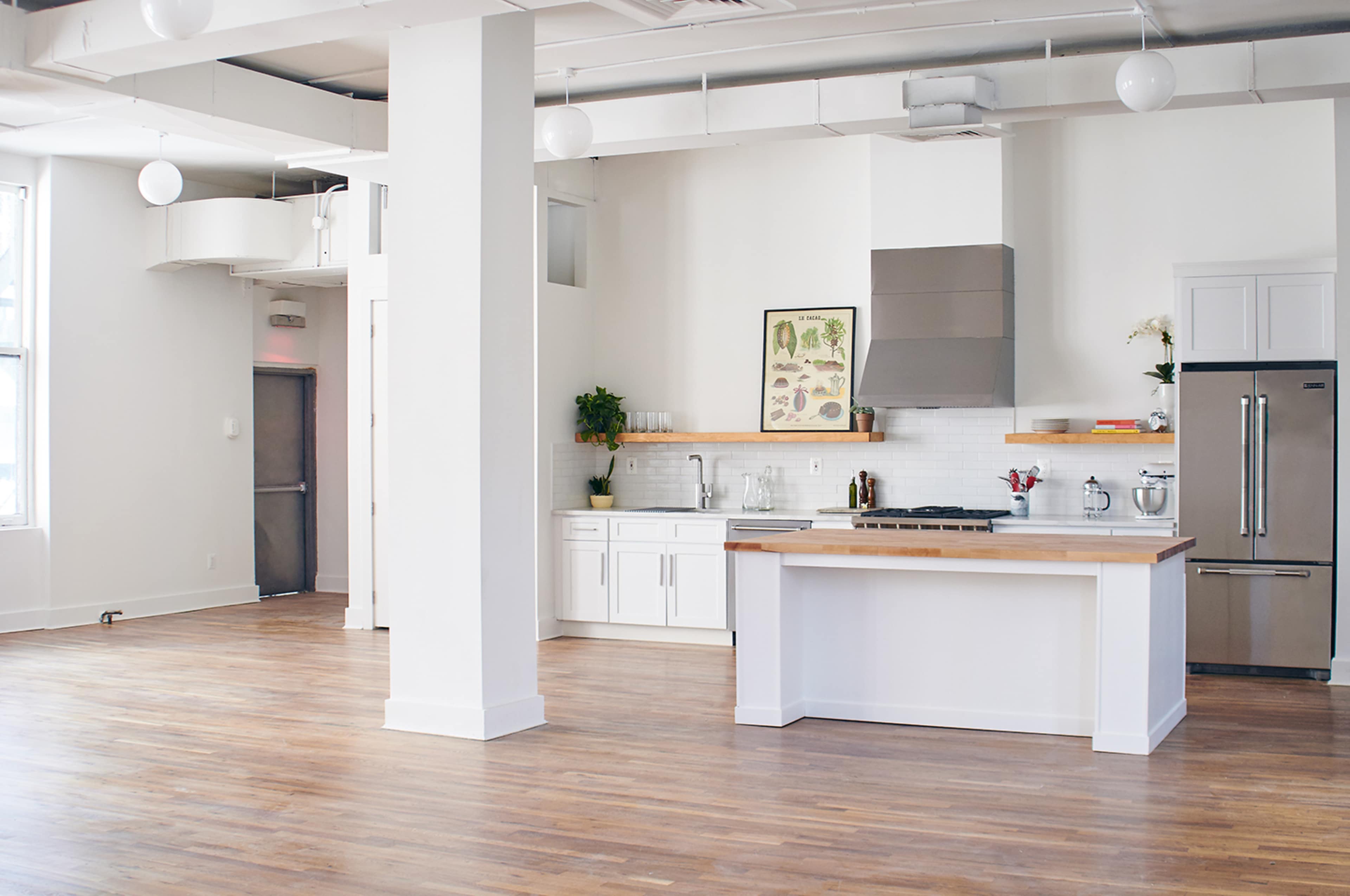 A modern kitchen with a central island, white cabinetry, and wooden countertops in a spacious, brightly lit room.