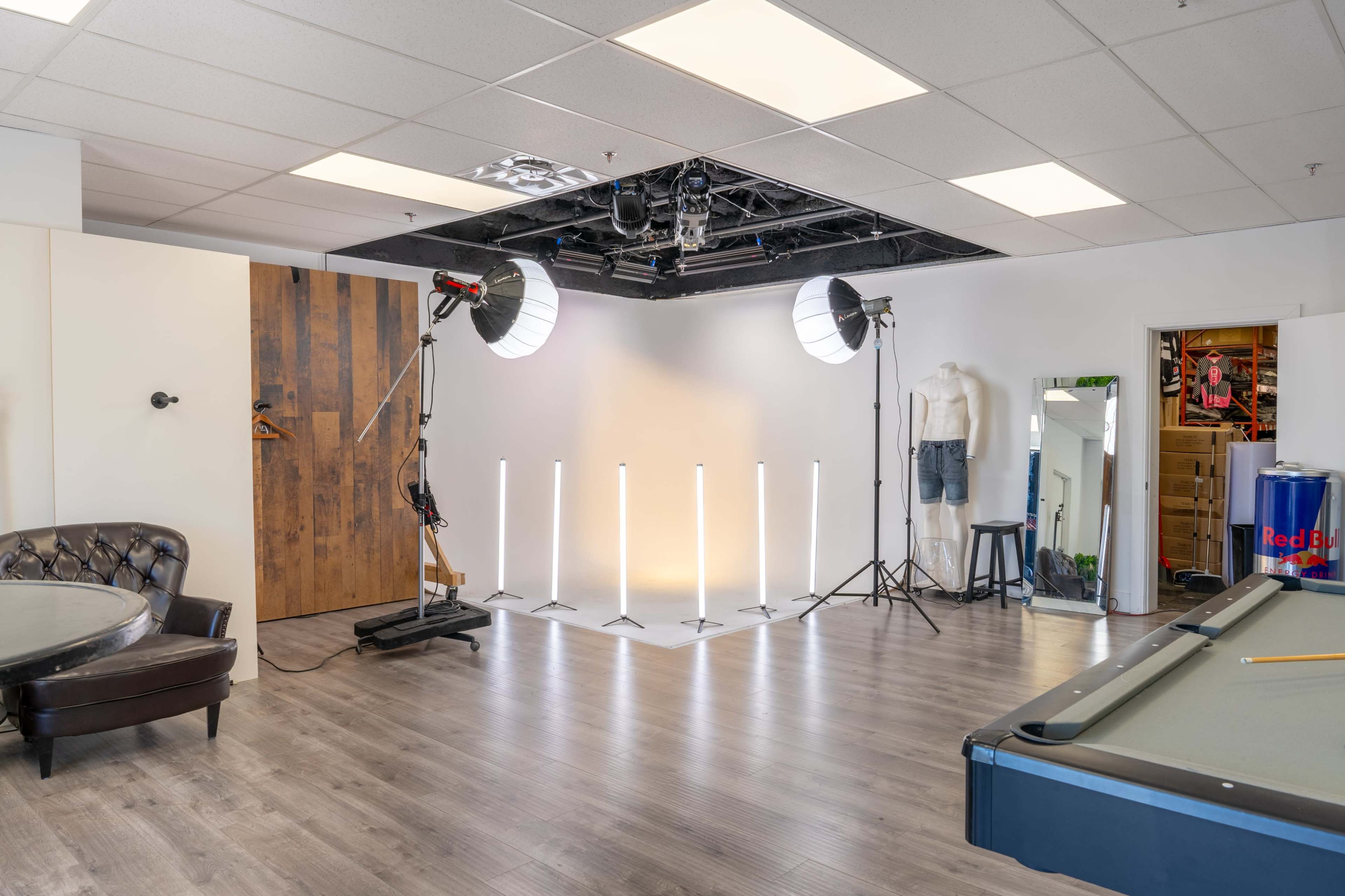 The image shows a photography studio equipped with lighting setups, a wooden door, a pool table, and various props.