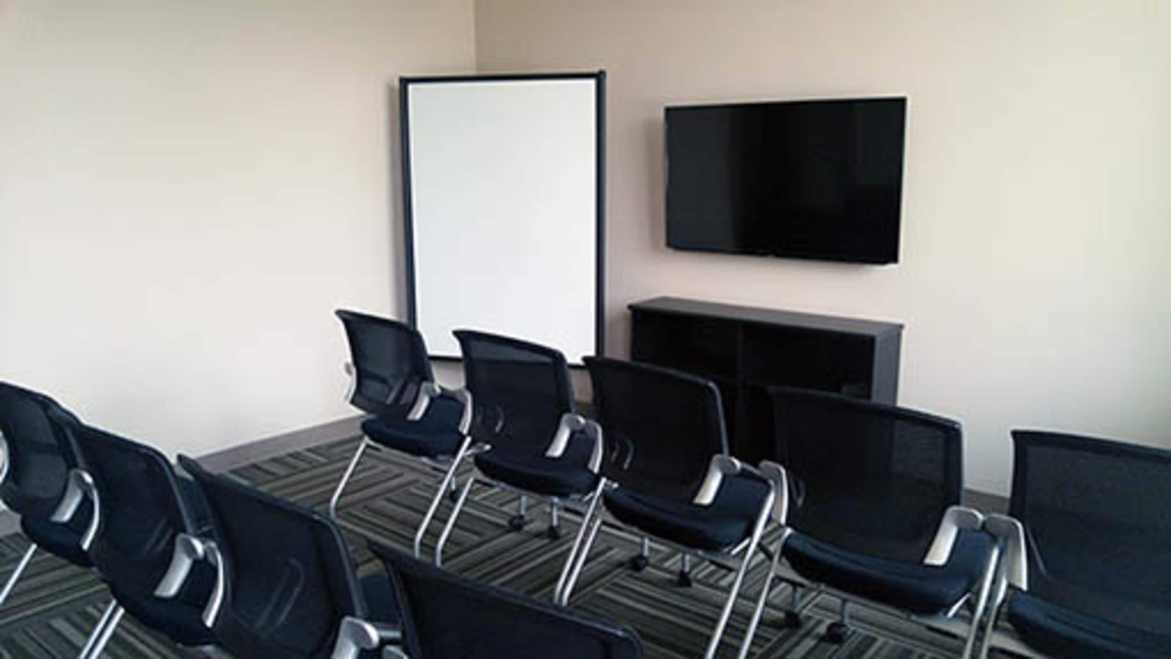 A meeting room is set up with several black chairs facing a wall-mounted television and a movable whiteboard.