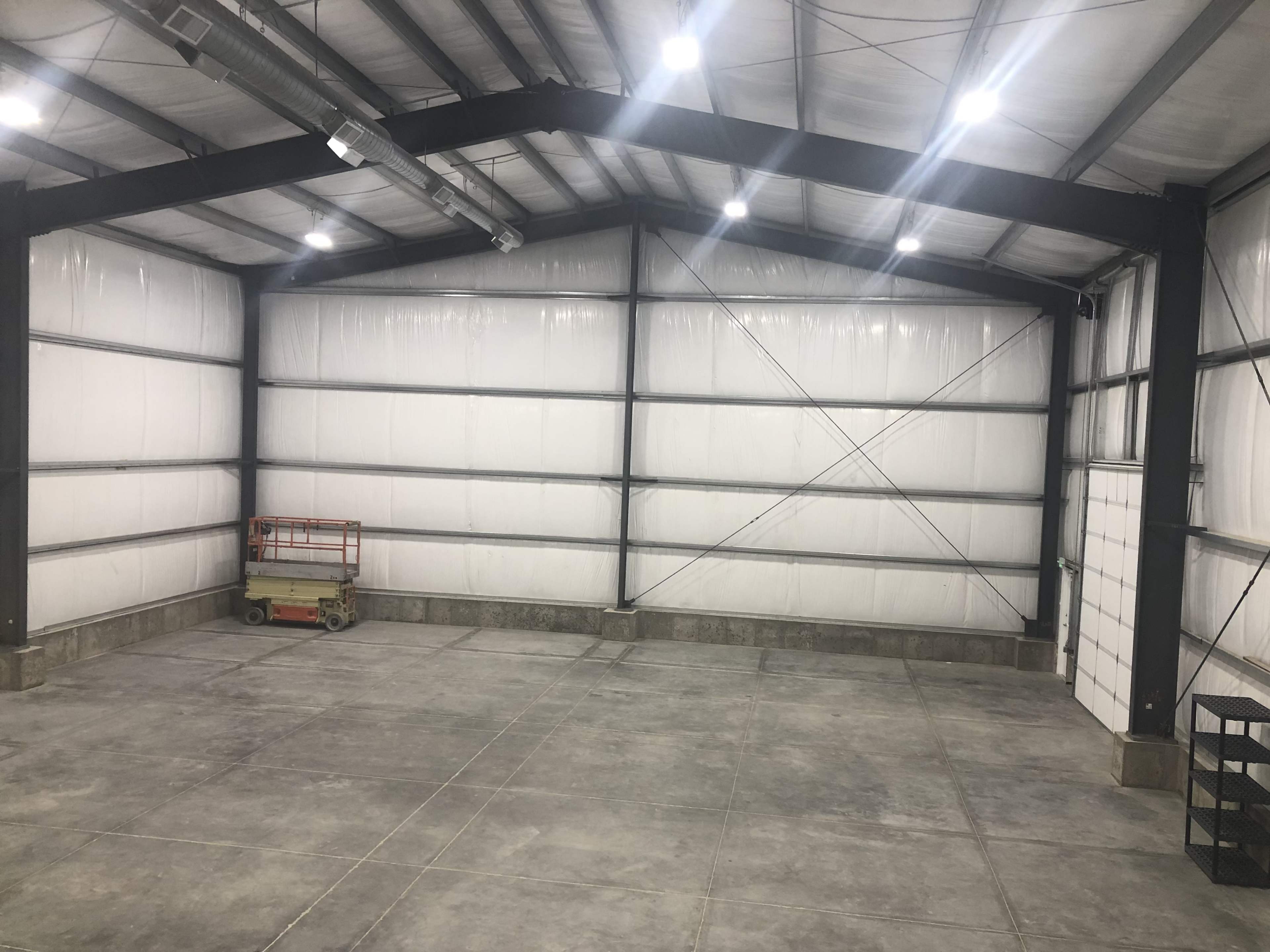 The interior of a large industrial warehouse with white walls, concrete flooring, and high ceilings supported by metal beams.