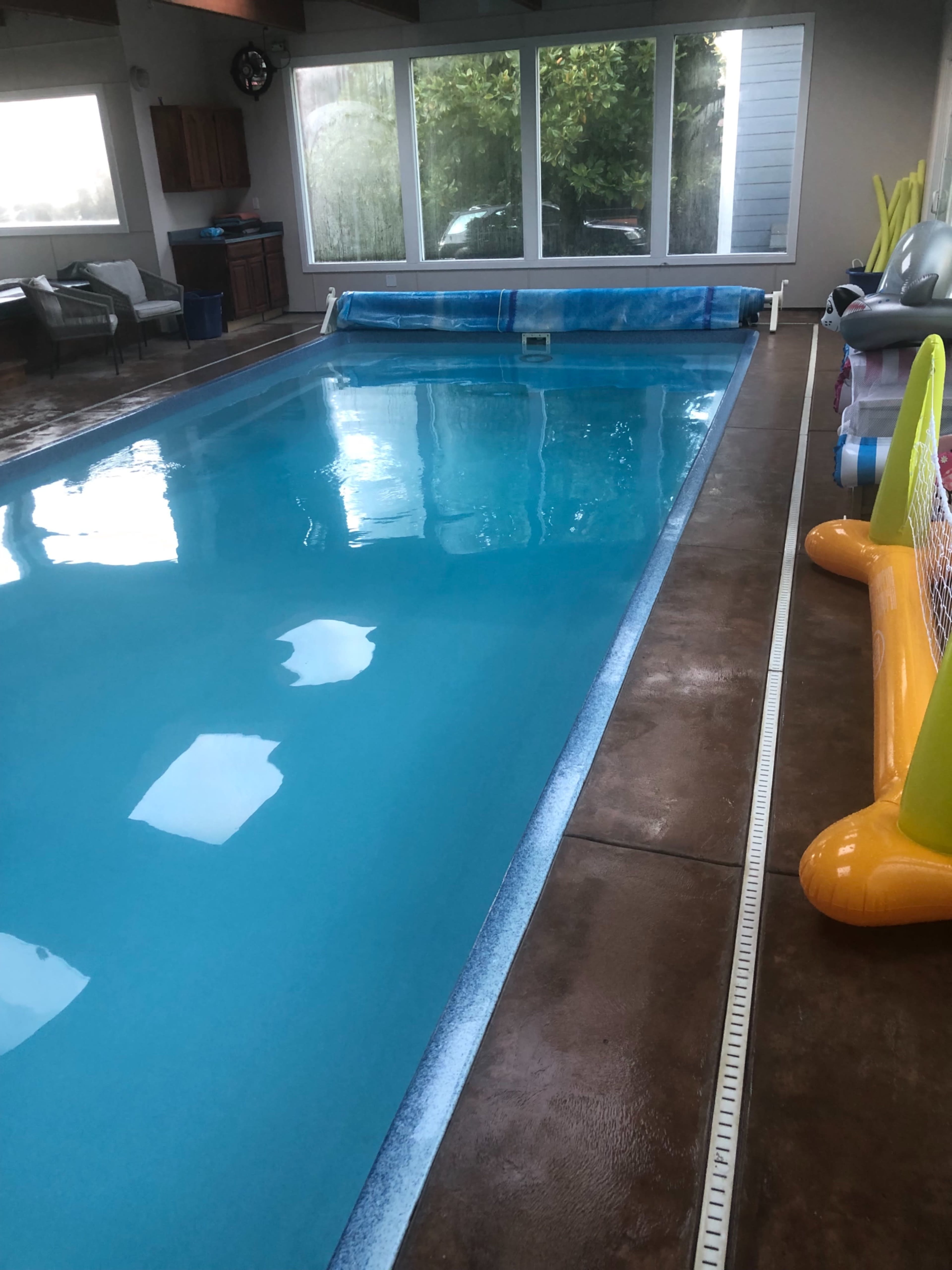 An indoor swimming pool with a clear blue surface, surrounded by a tiled deck and several poolside accessories.
