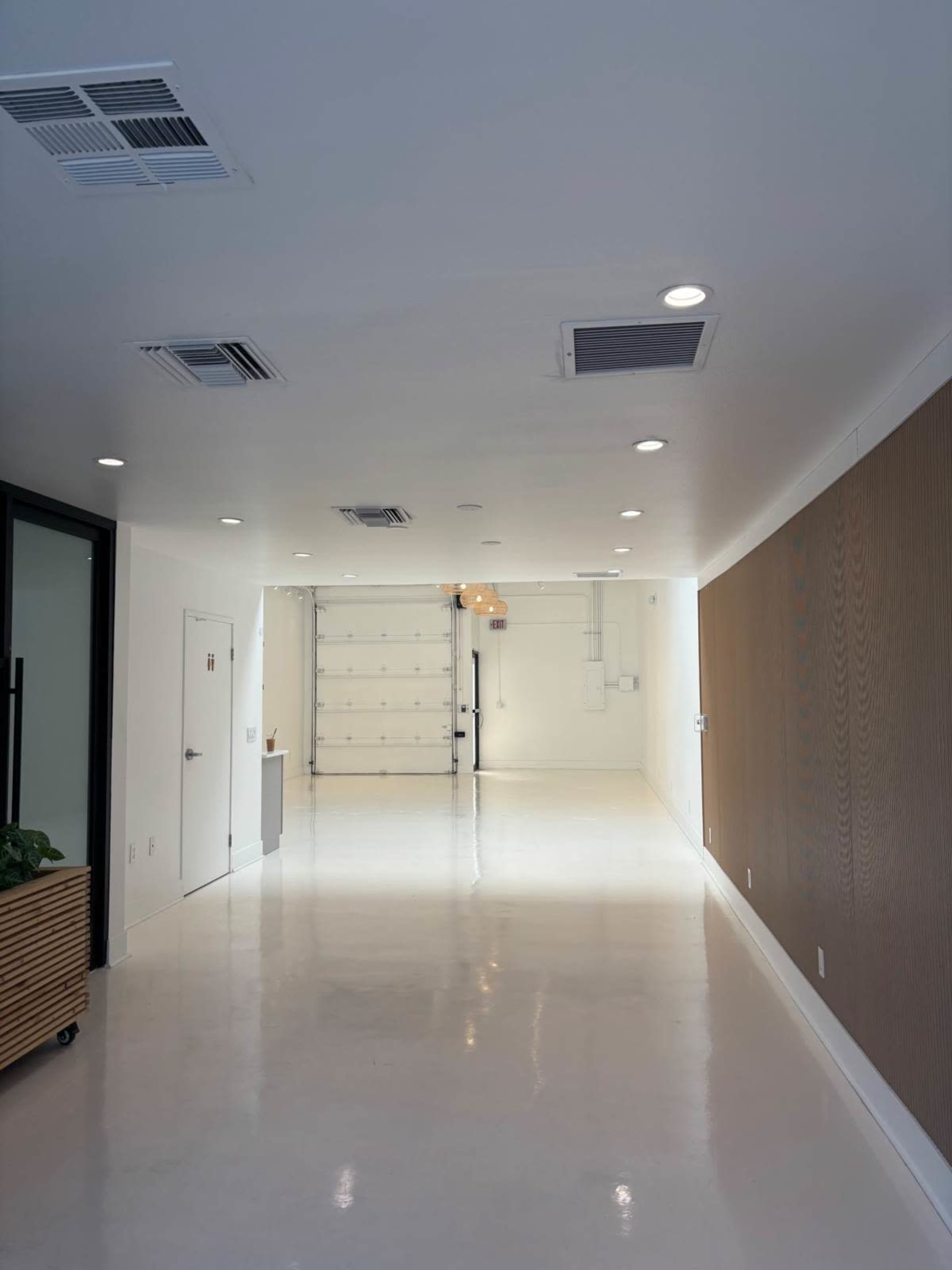 The image shows a spacious, well-lit room with white walls, a light-colored floor, and a garage door at the far end.