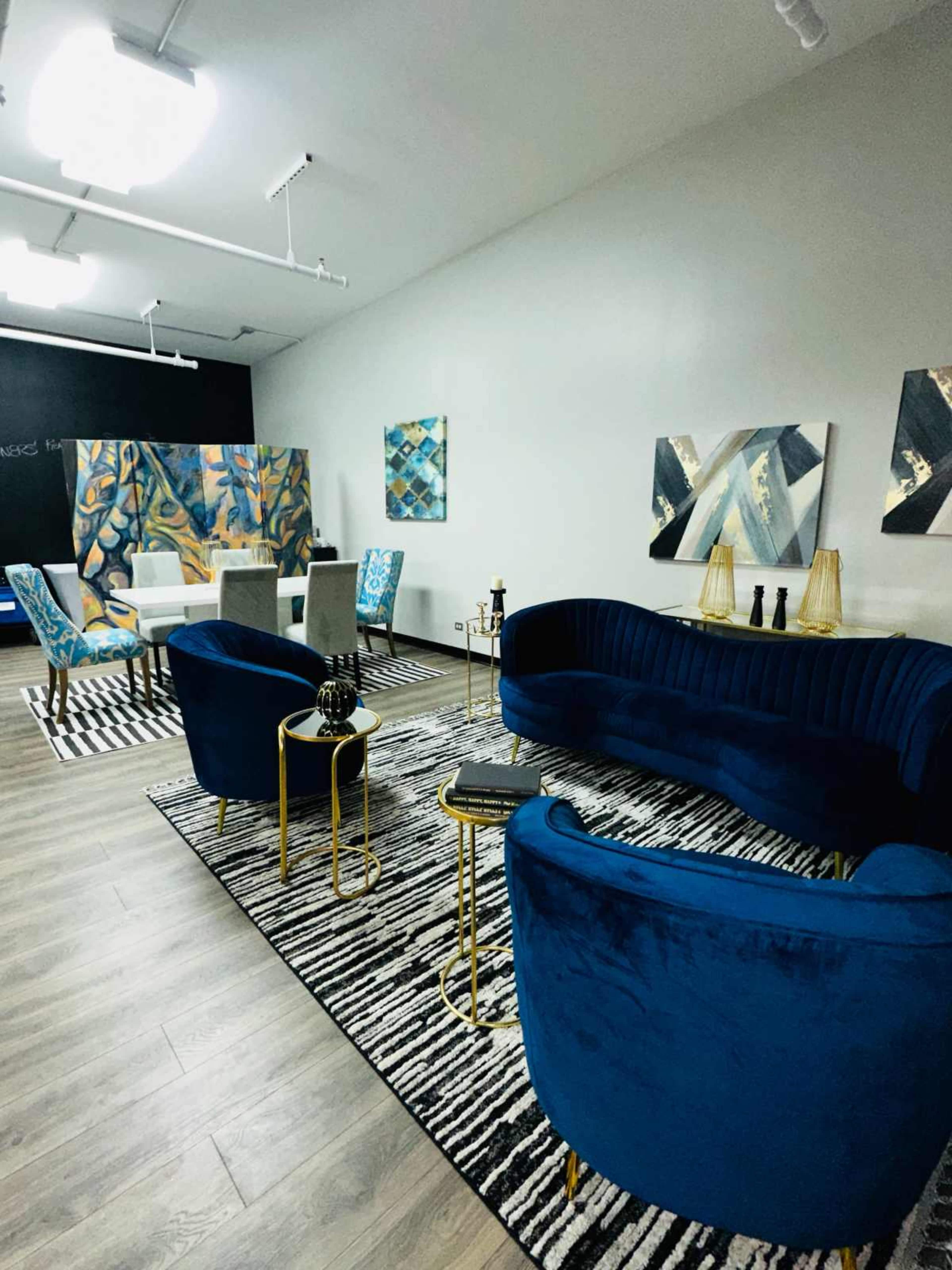 A modern lounge area with blue velvet sofas, gold accents, and abstract artwork on the walls, complemented by a striped area rug.