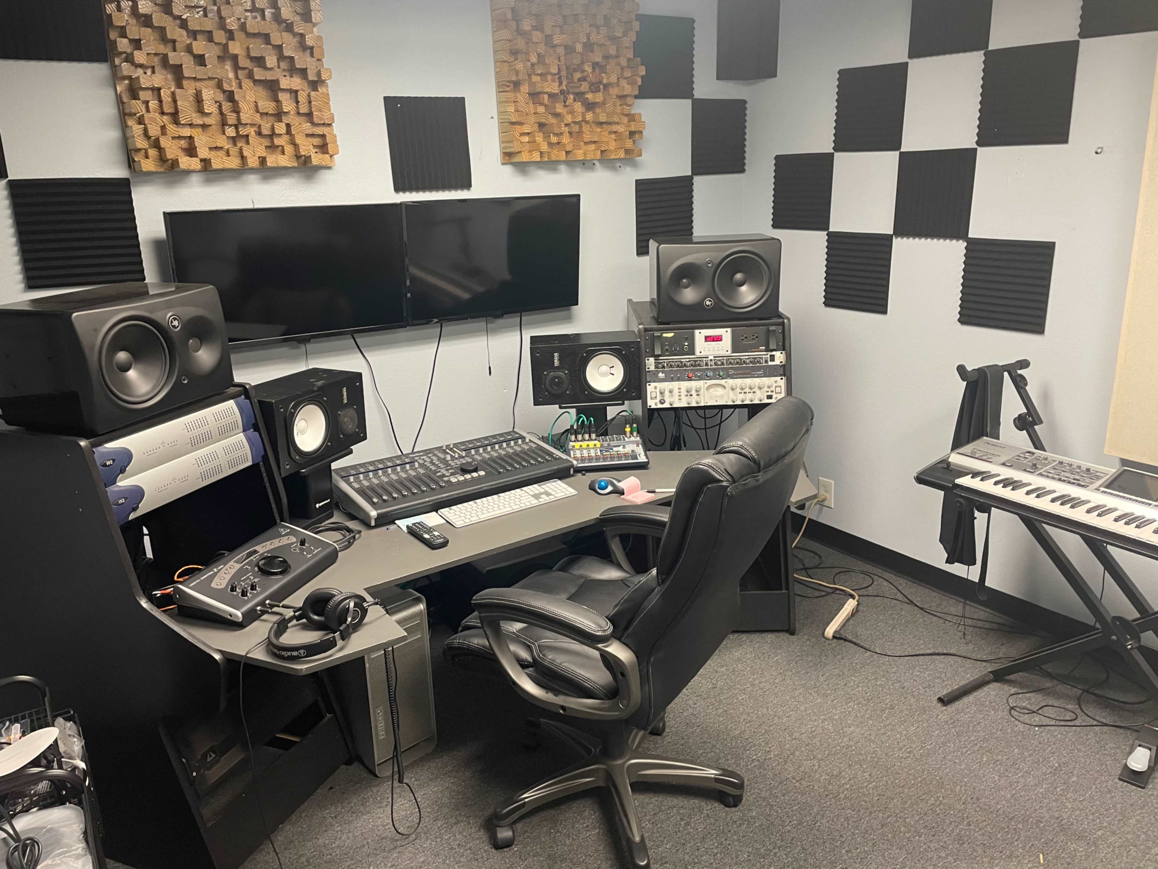 A home music production studio featuring a computer desk with audio equipment, speakers, and a keyboard.