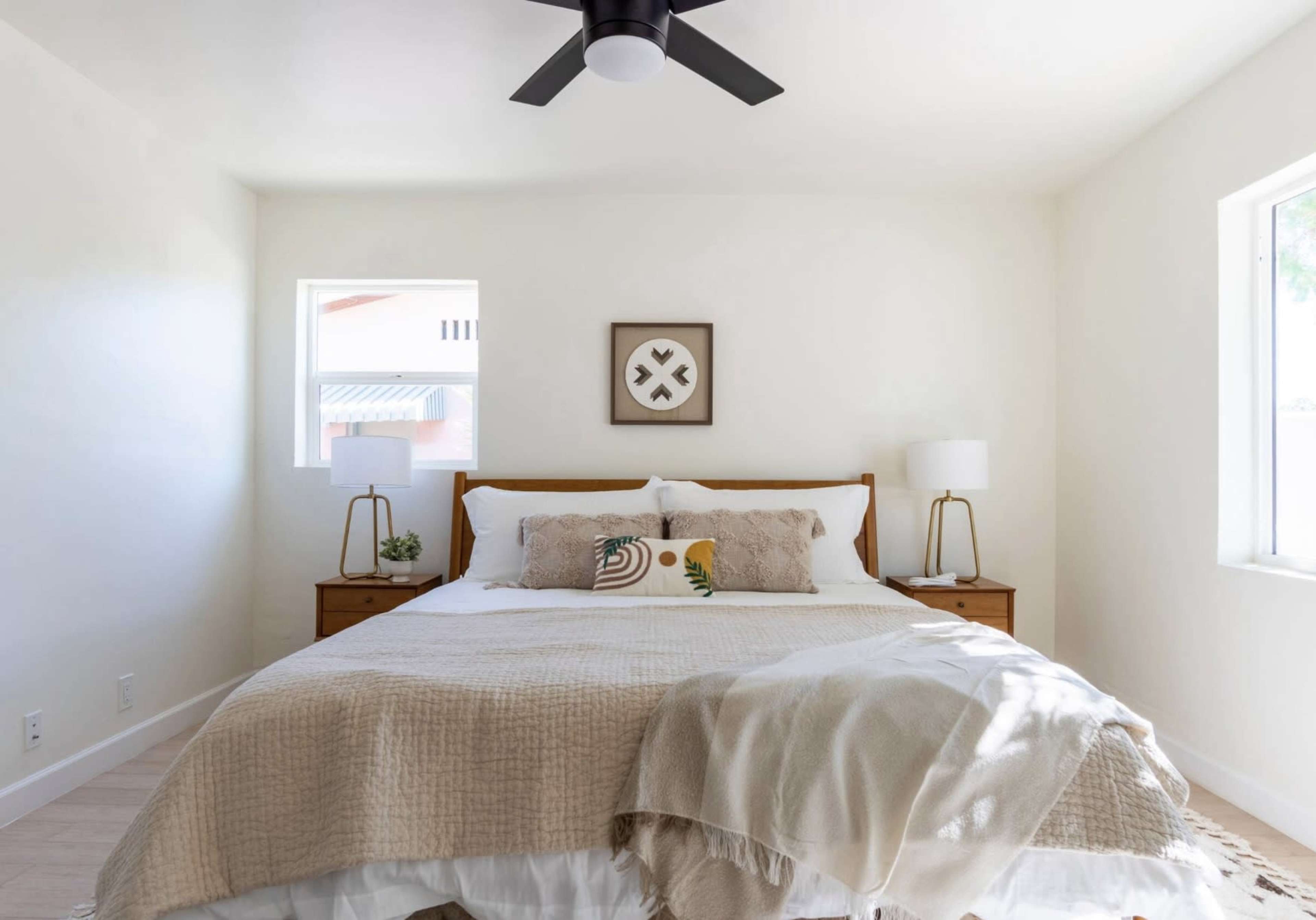 A neatly arranged bedroom featuring a bed with neutral-colored bedding, two bedside lamps, and a minimalistic wall decoration.