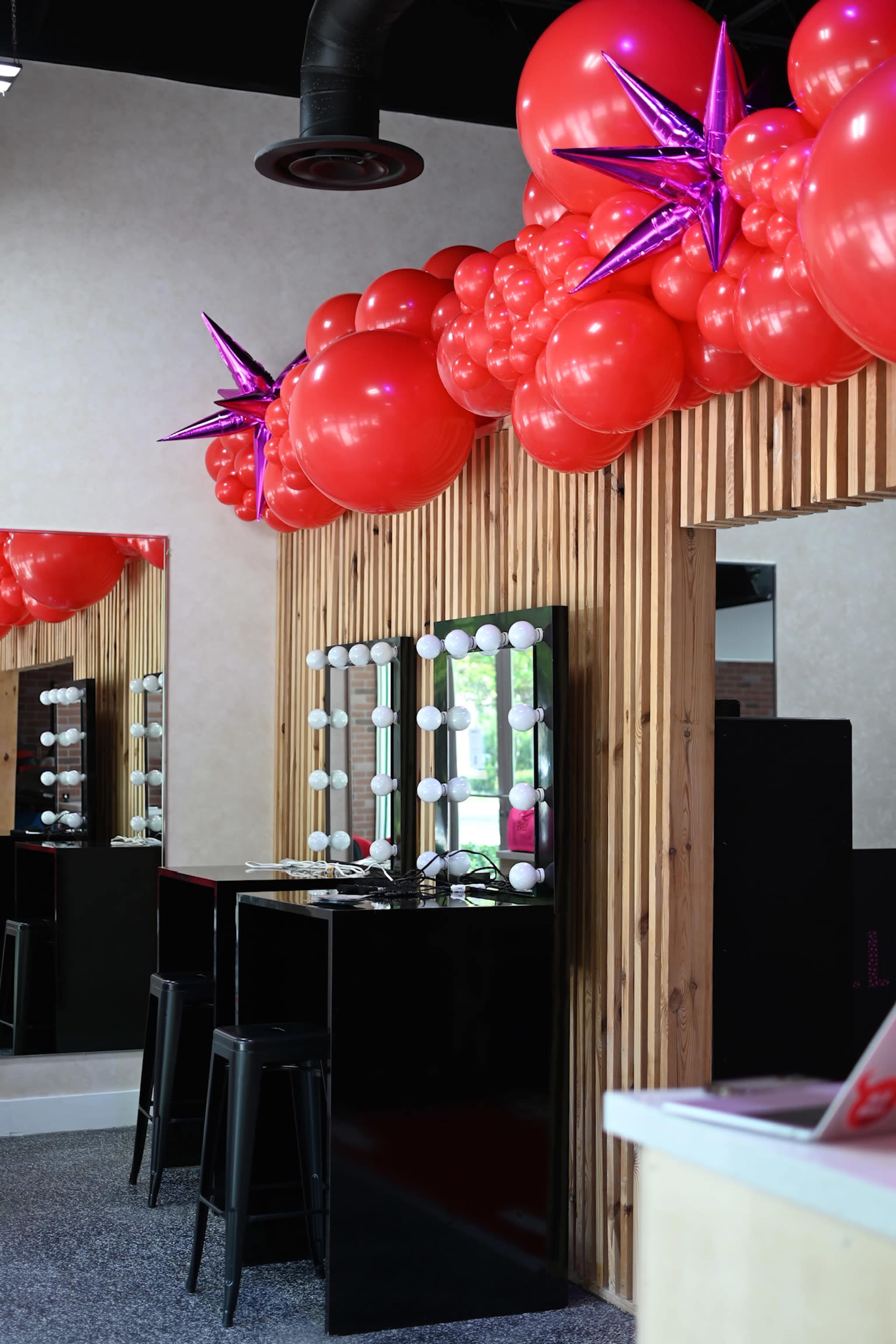 A stylish vanity area with black furniture and a decorative display of red balloons and star accents above a series of illuminated mirrors.