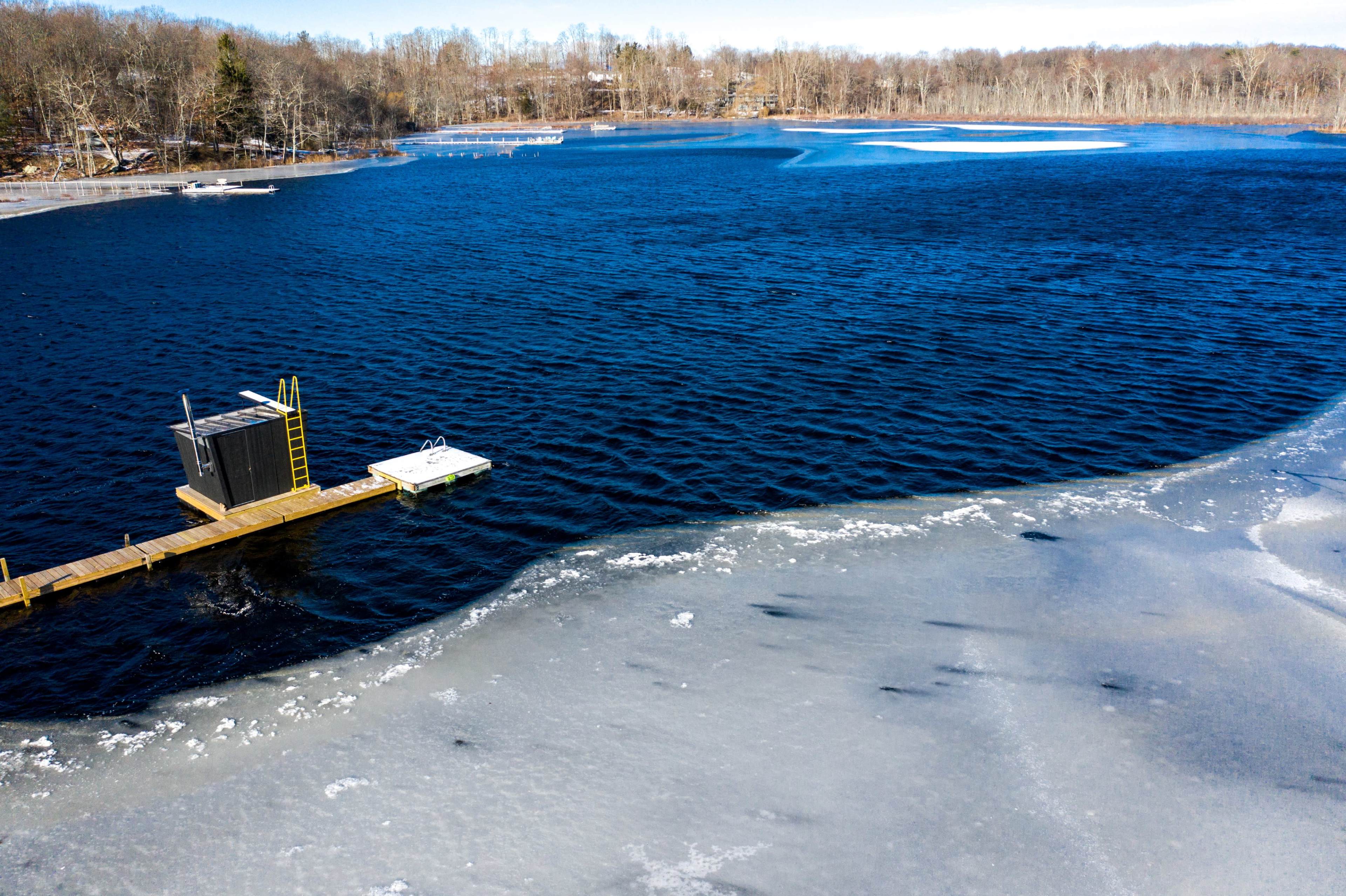 A wooden dock extends into a partially frozen lake surrounded by trees in early winter.