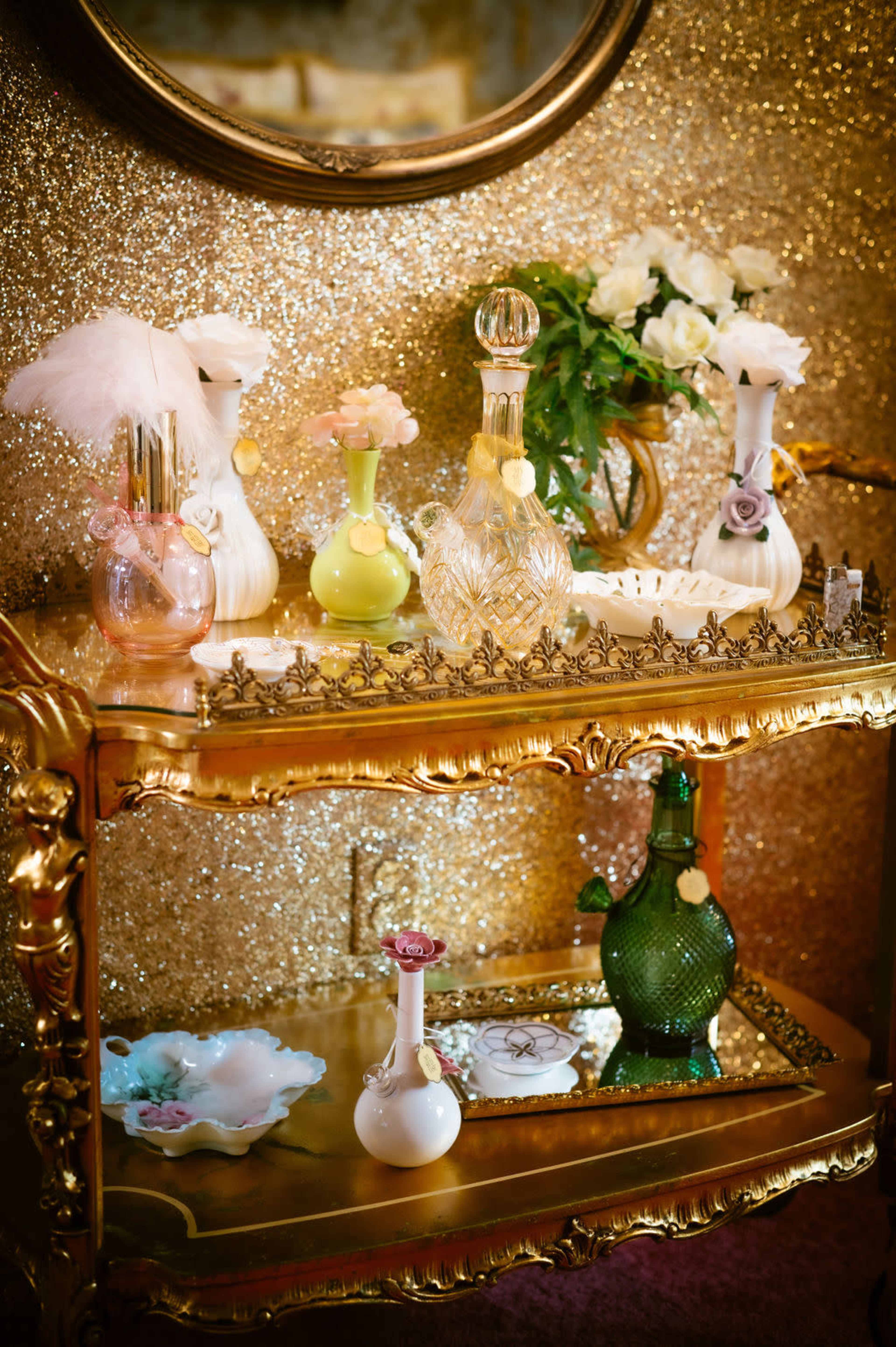A golden serving cart displays various decorative perfume bottles and a small floral arrangement against a glittering background.