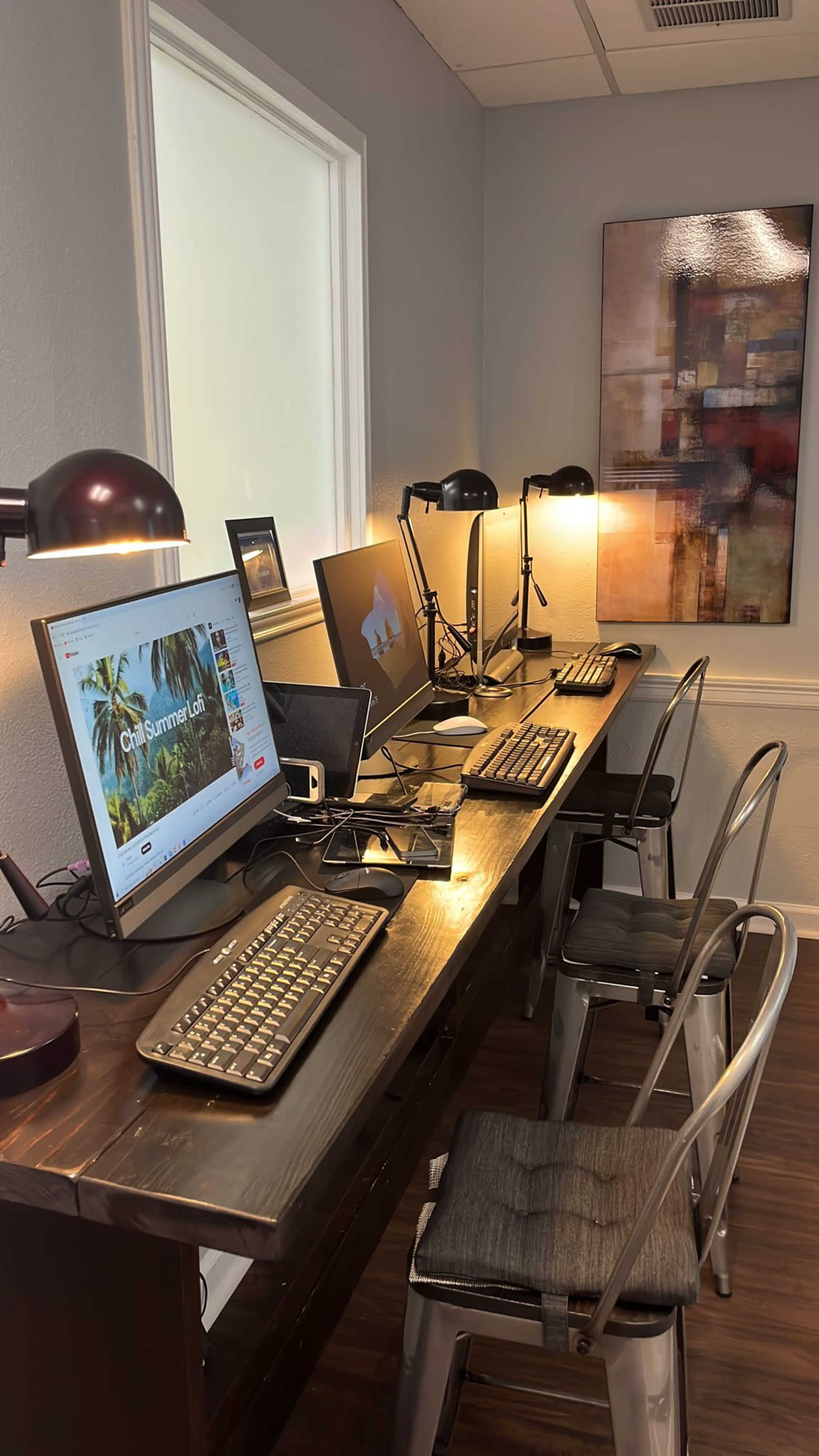 A row of four computers on a wooden table, each equipped with a keyboard, in a well-lit office space.