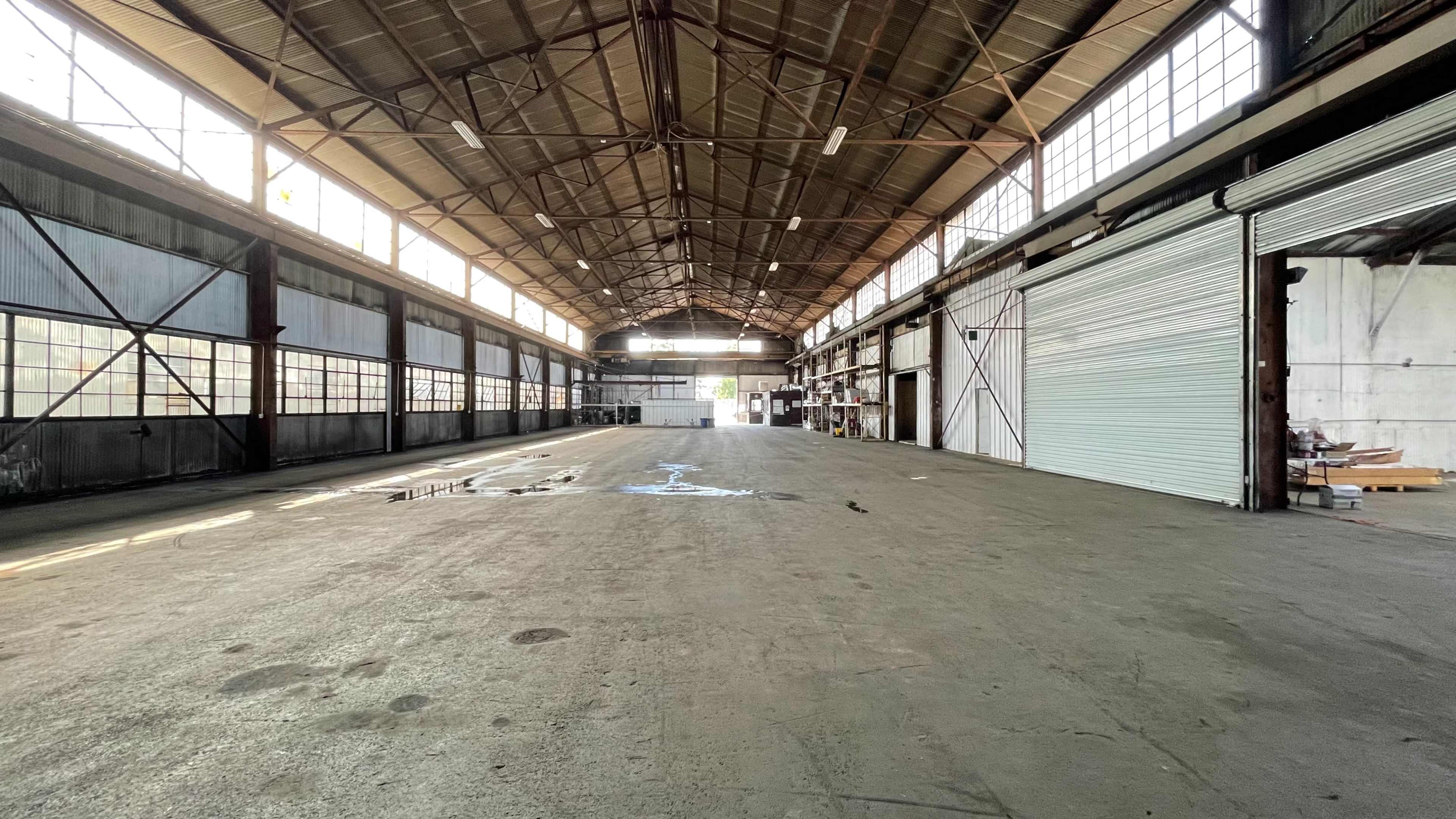 An empty industrial warehouse with large windows and a high ceiling.
