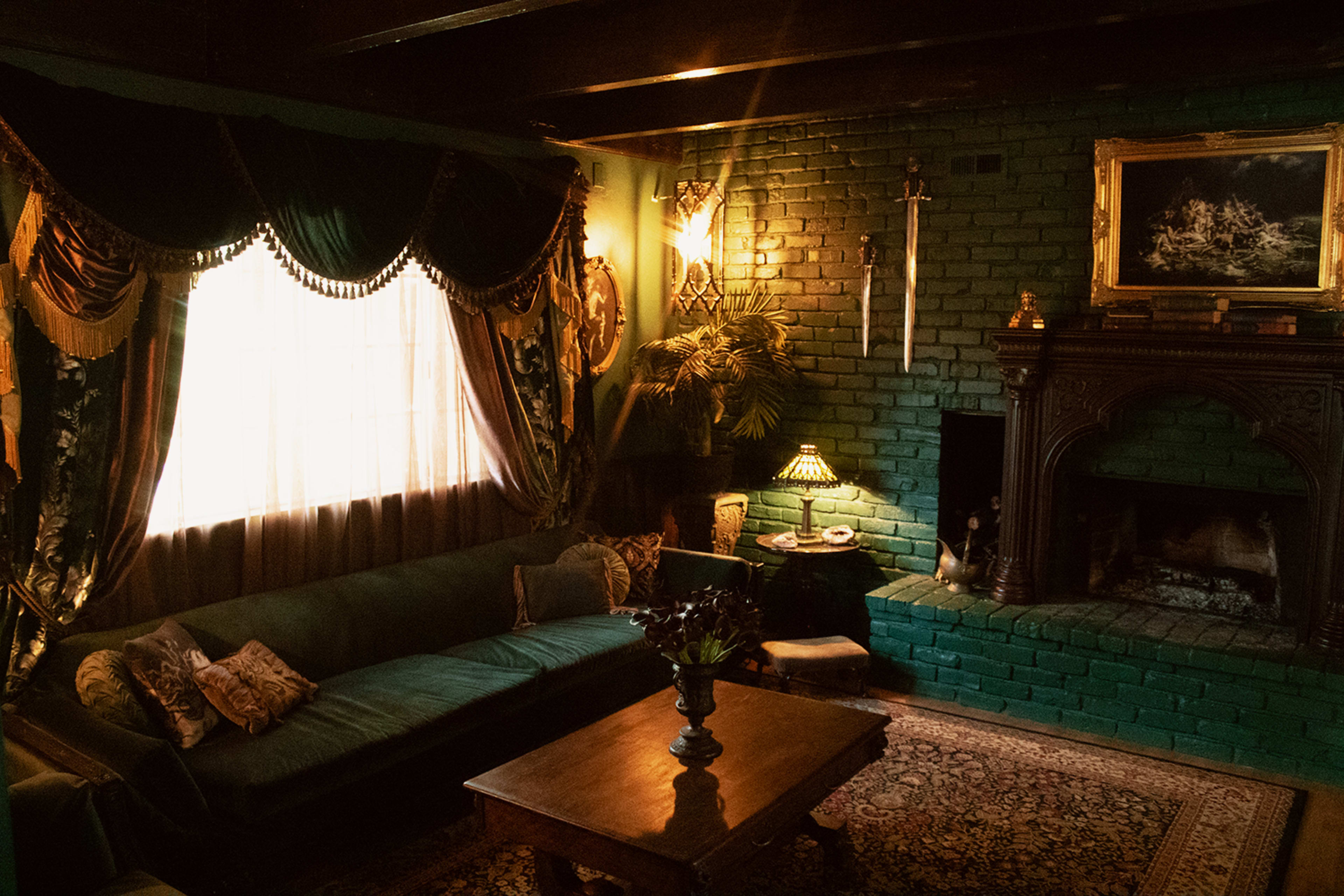 The image depicts a cozy living room with a green brick wall, a dark wooden fireplace, a patterned rug, and a dark green sofa adorned with pillows.