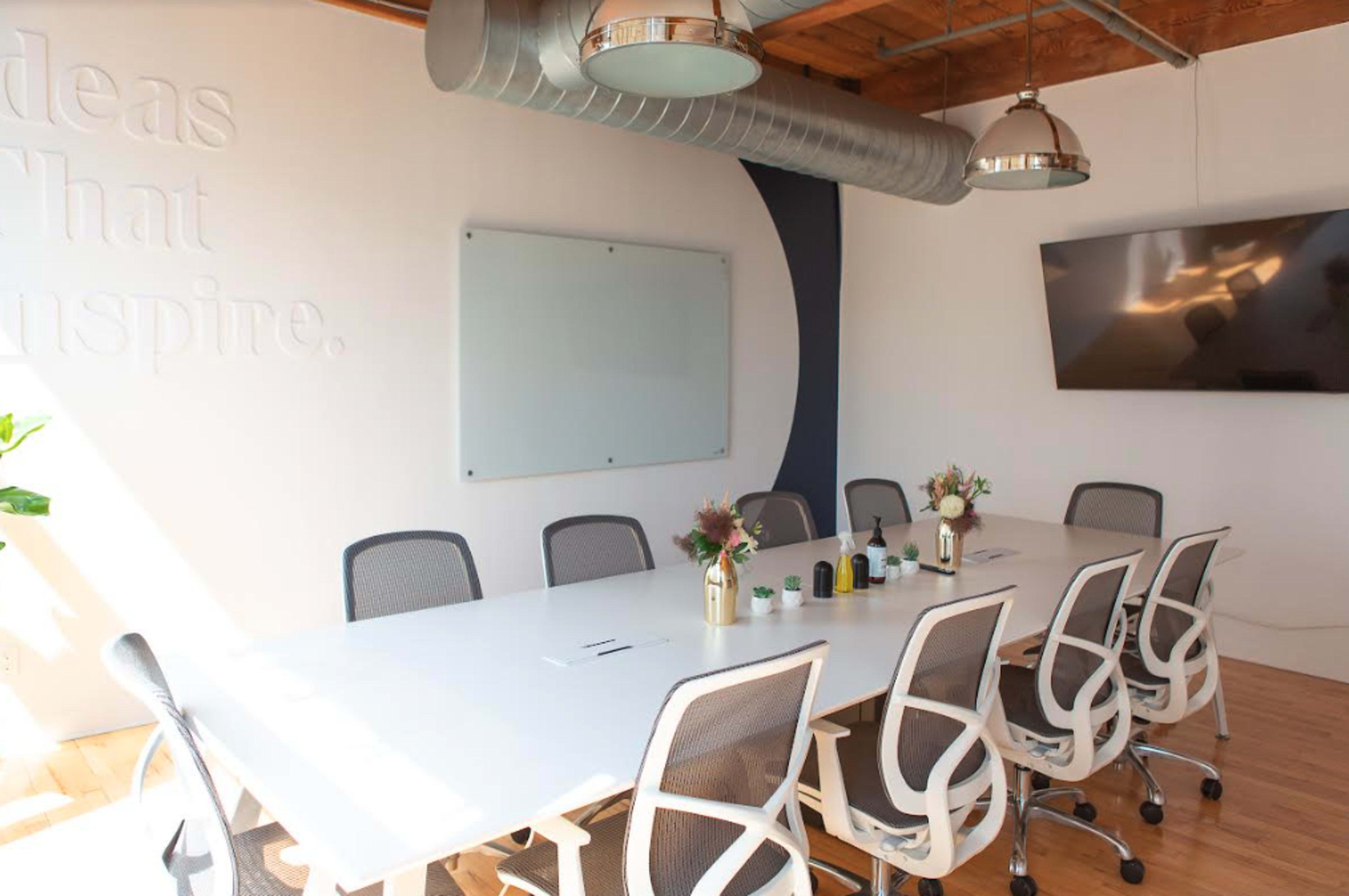 A large conference room features a long white table with rolling chairs, a wall-mounted screen, and a whiteboard.