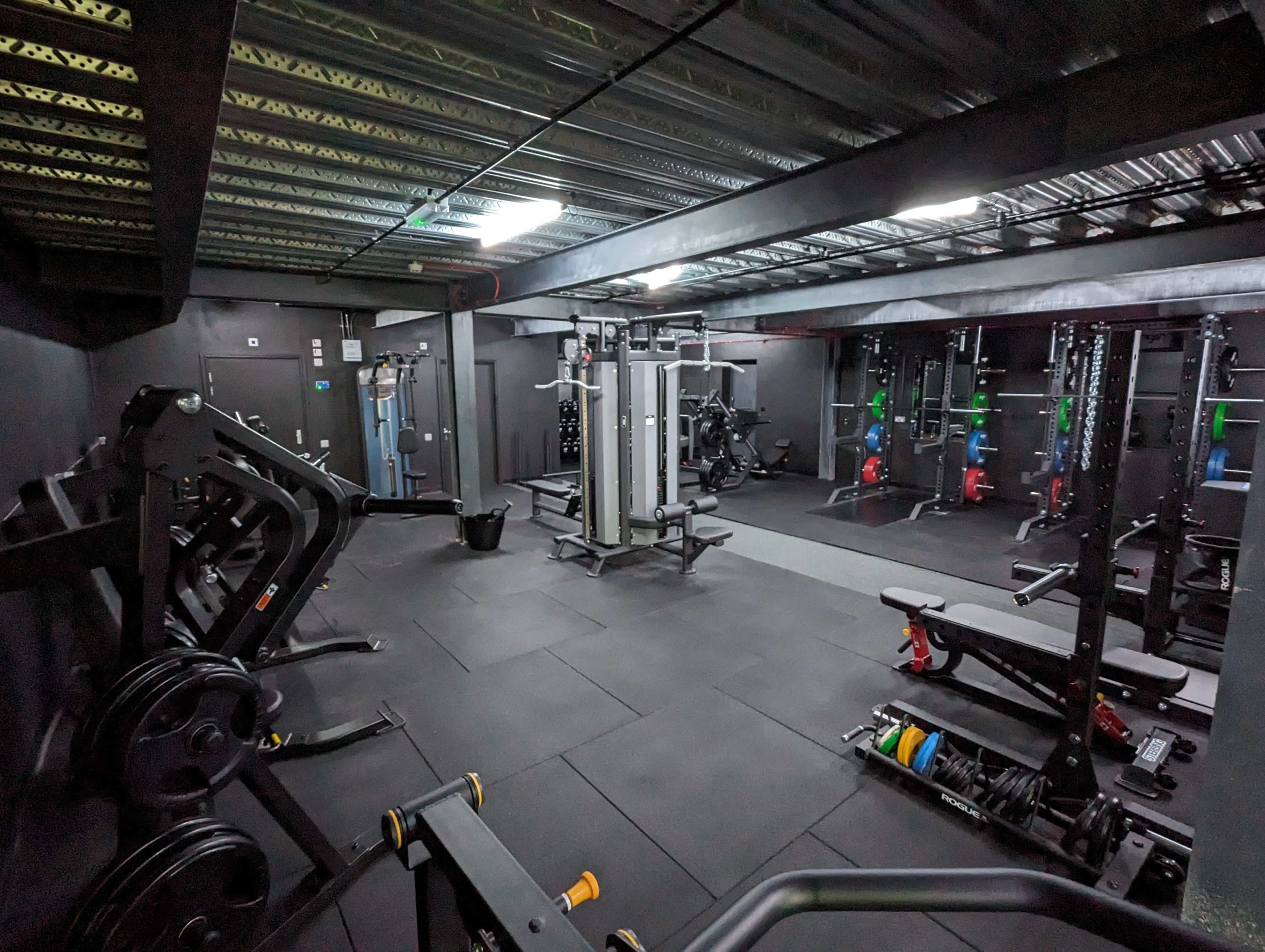 A well-equipped gym with various weightlifting machines and benches arranged in a black-floored space.