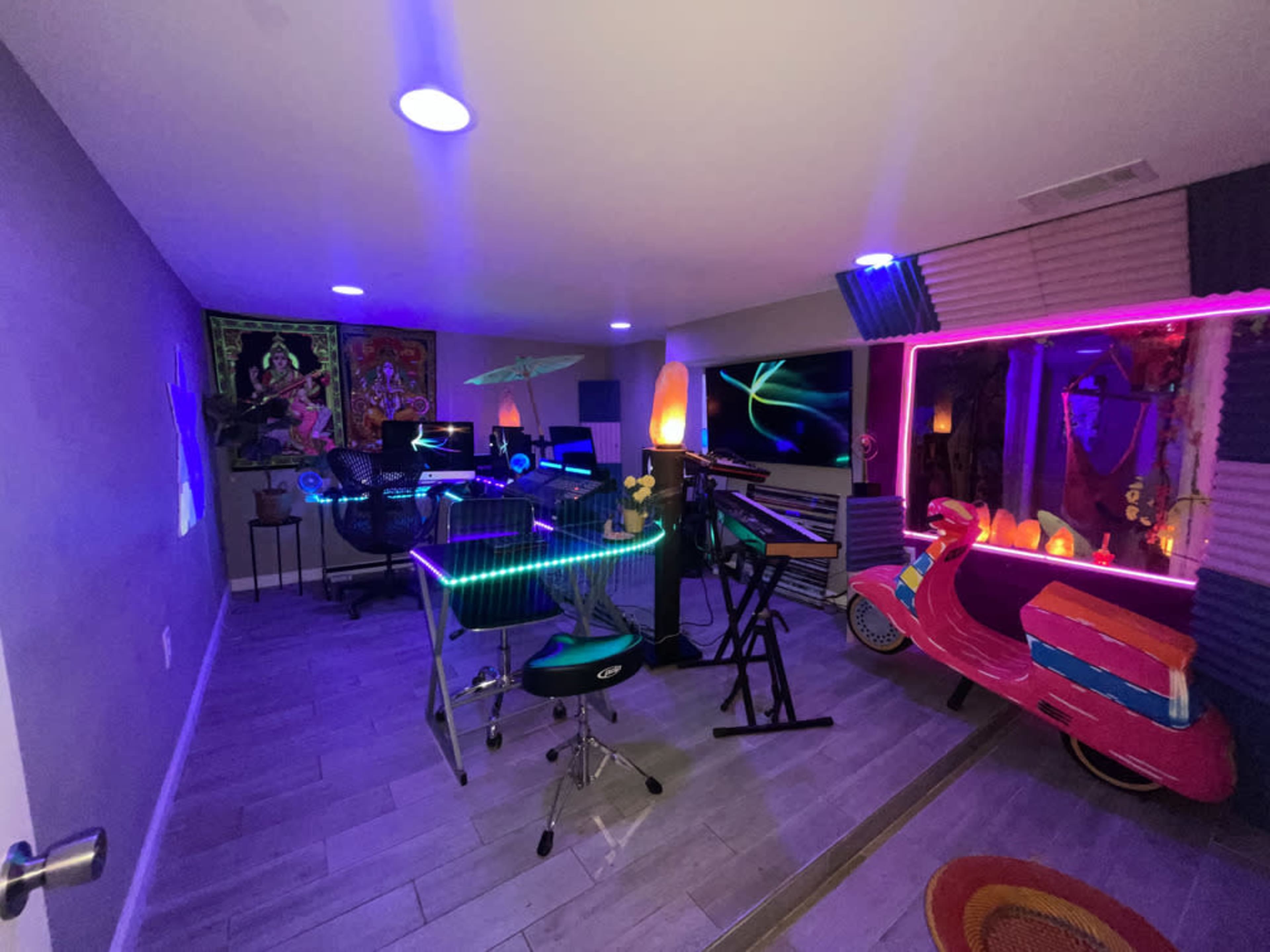 A colorful room filled with modern furniture, musical instruments, and neon lighting, including a brightly decorated vehicle.
