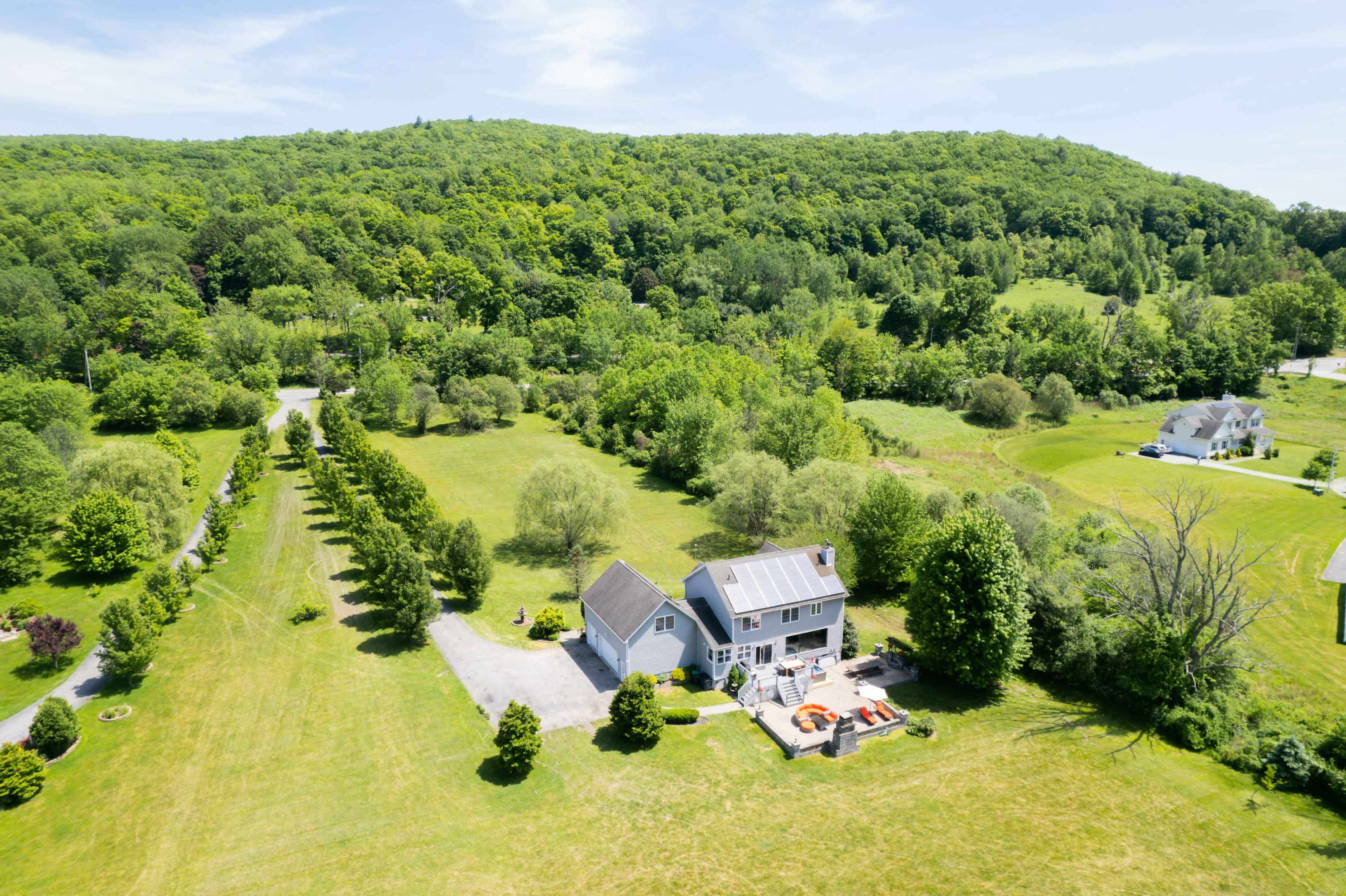A spacious house with a large yard is surrounded by trees and hills in a rural landscape.