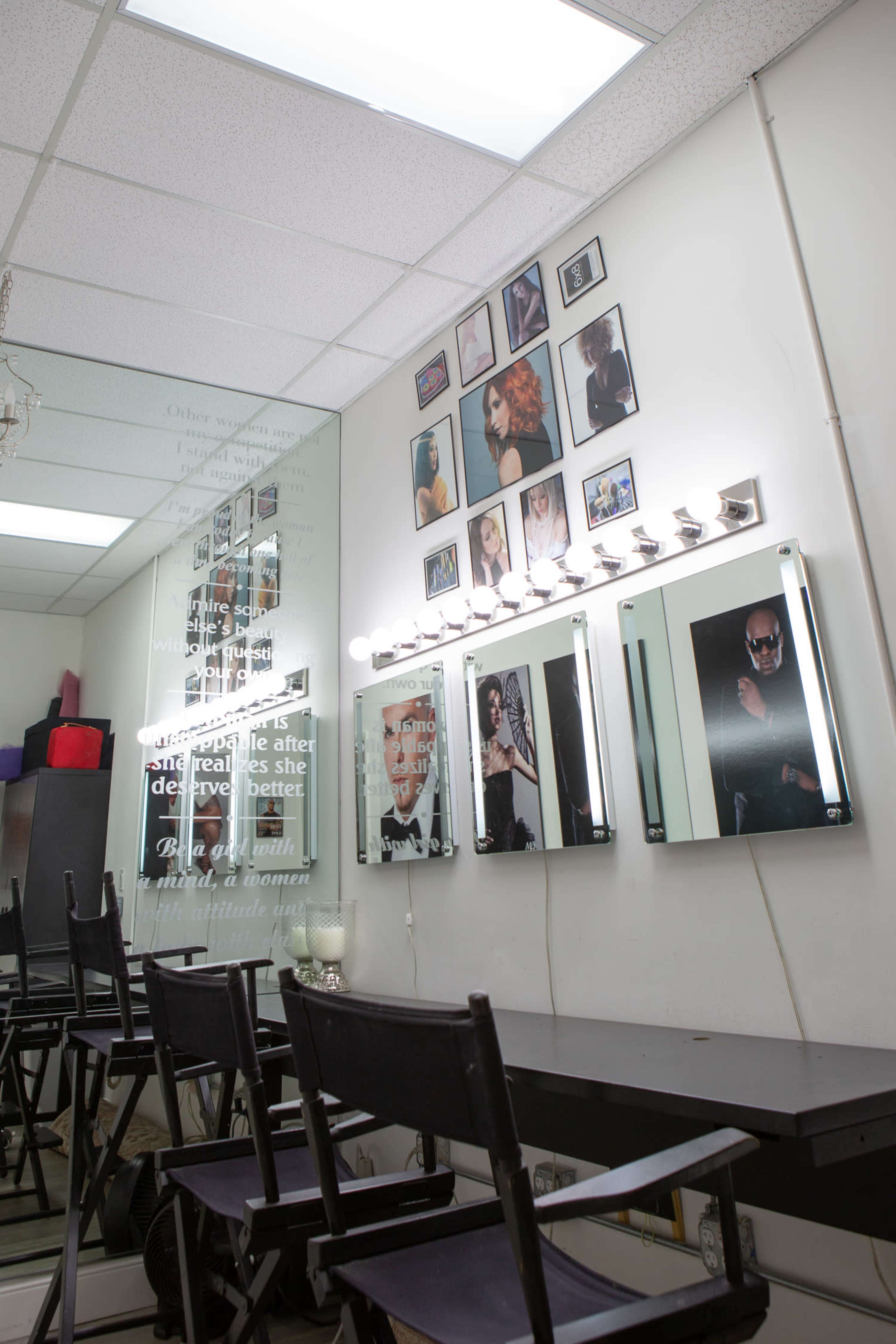 The image shows a makeup studio with mirrors and framed photographs on the wall, complemented by black chairs and a long table.