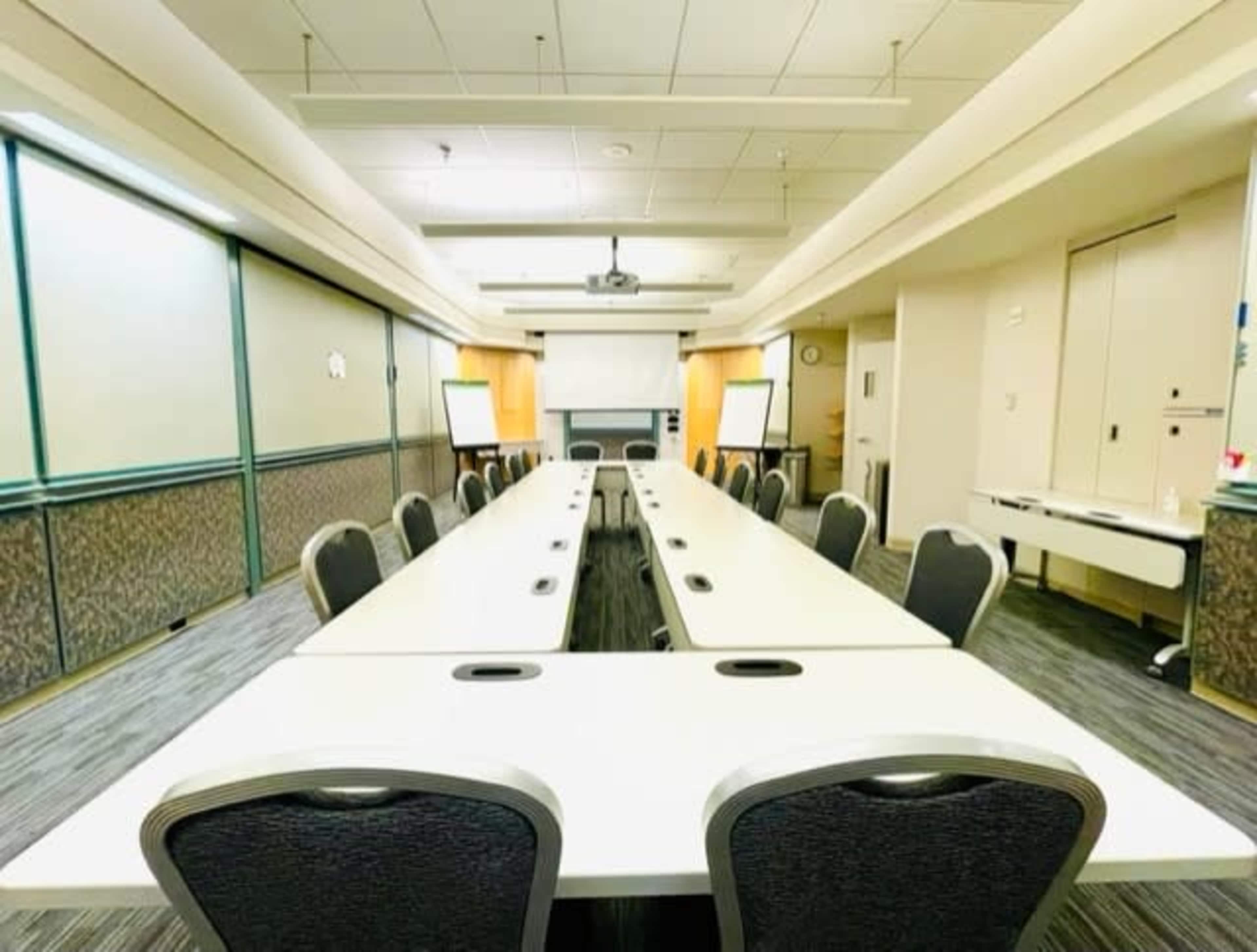 A large conference room features long tables arranged in a U-shape with chairs and presentation equipment at one end.