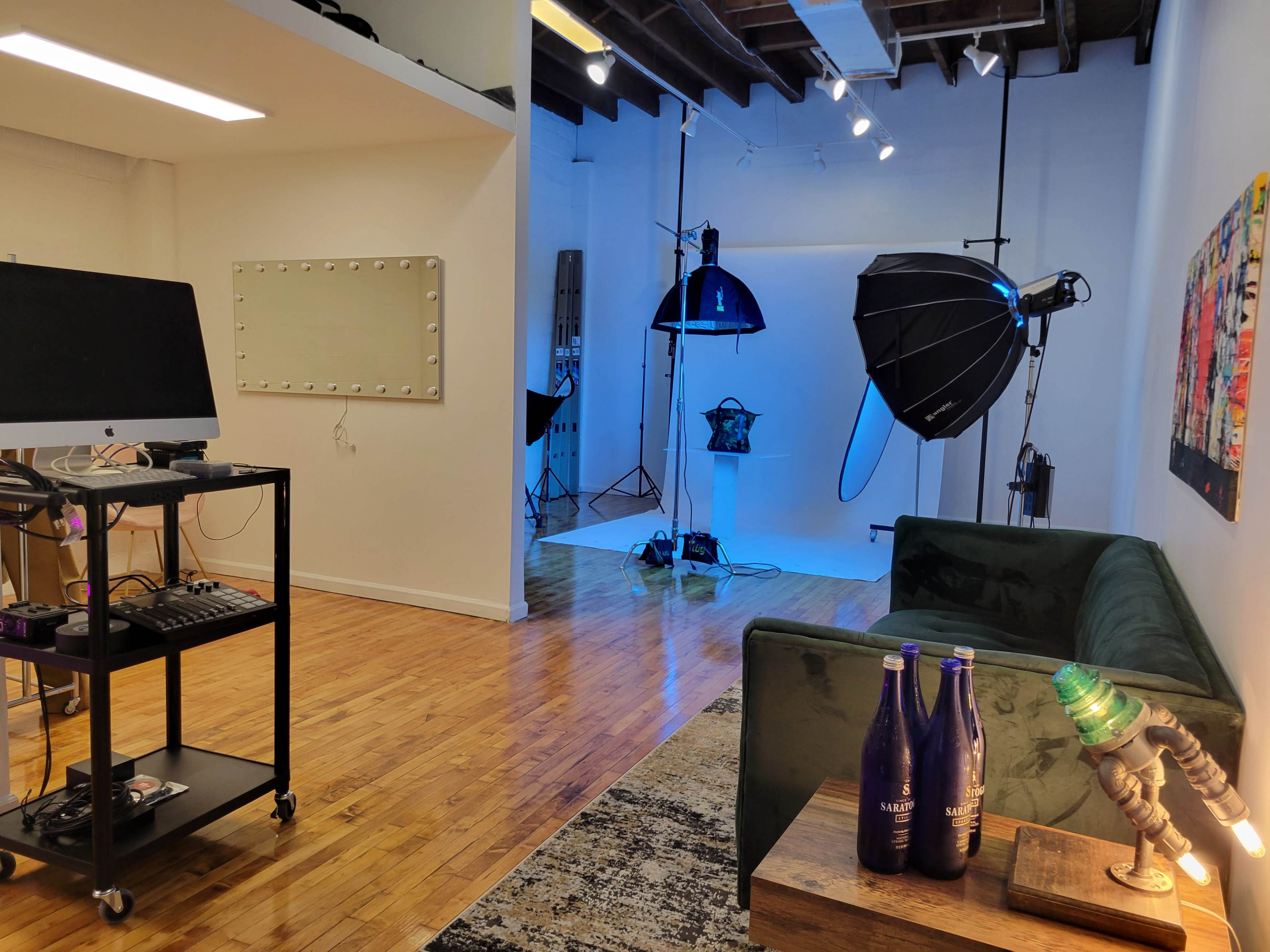 The image shows a studio space with a green sofa, photography lighting equipment, and a computer setup on a rolling cart.