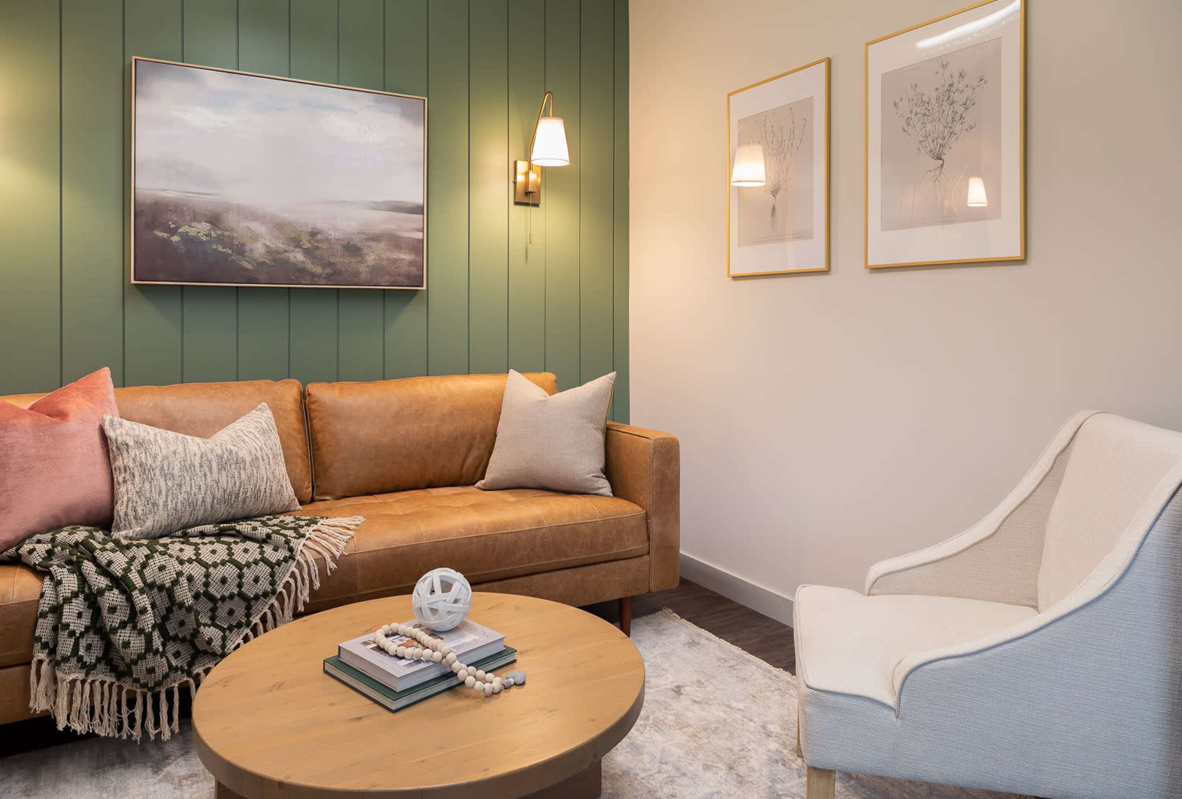 A modern living room featuring a brown leather sofa with decorative pillows, a round wooden coffee table, and framed artwork on the walls.