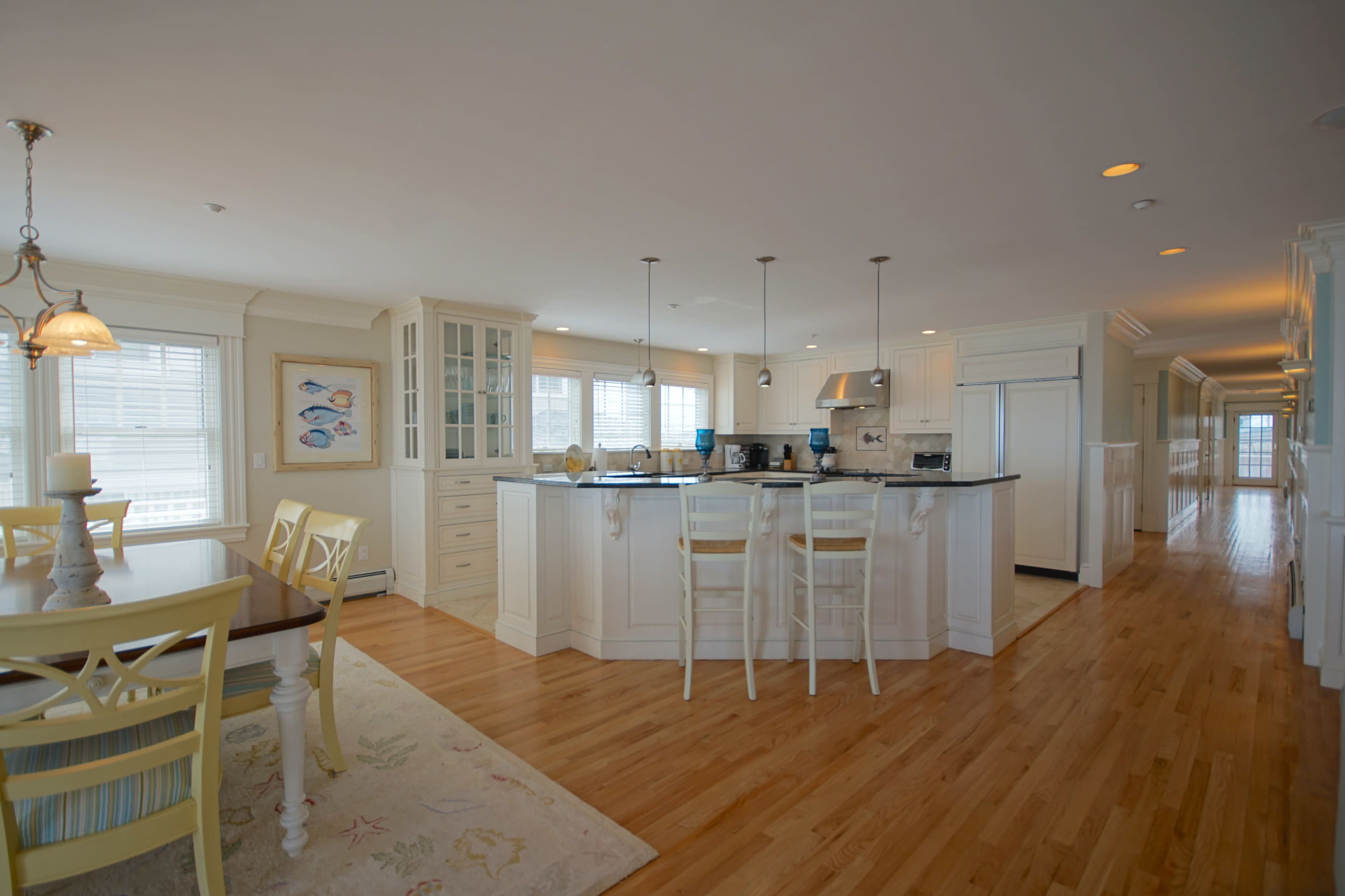A bright, open-concept kitchen and dining area with white cabinetry, a large island, and wooden flooring.