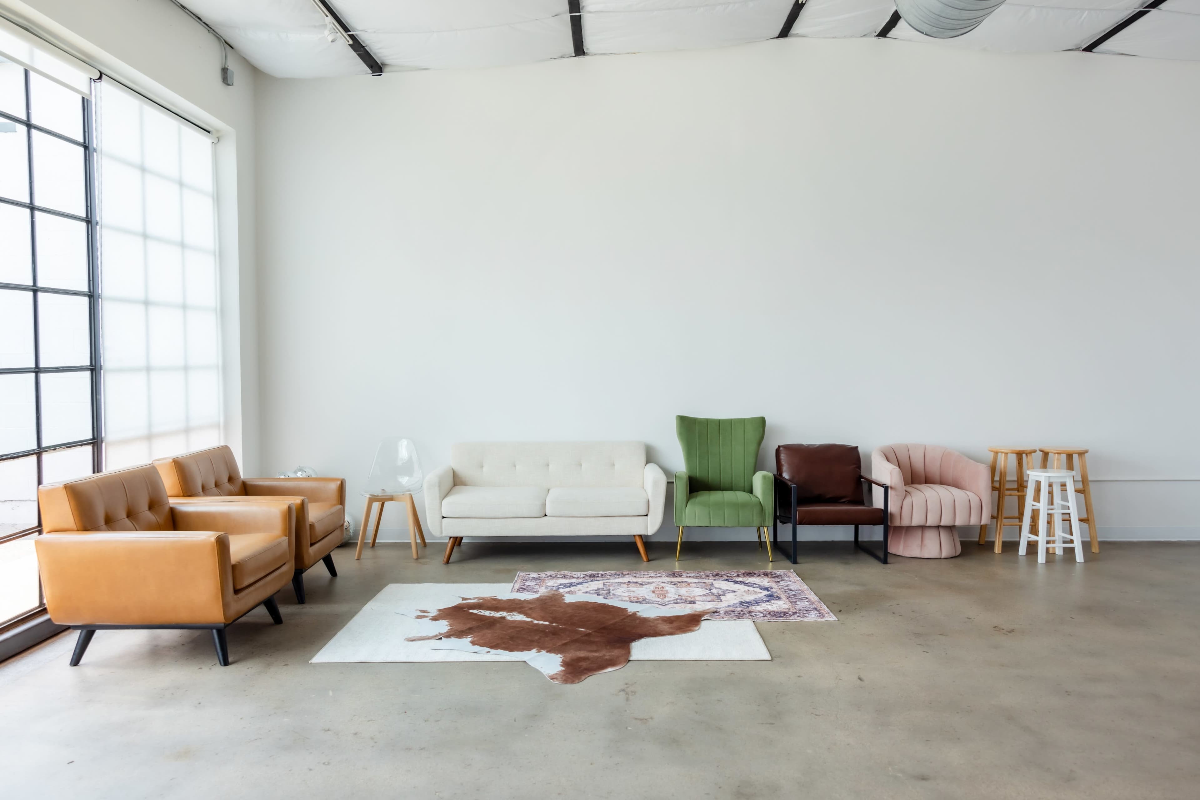 A minimalist room with a variety of seating options, including sofas and chairs, arranged on a concrete floor next to a large window.