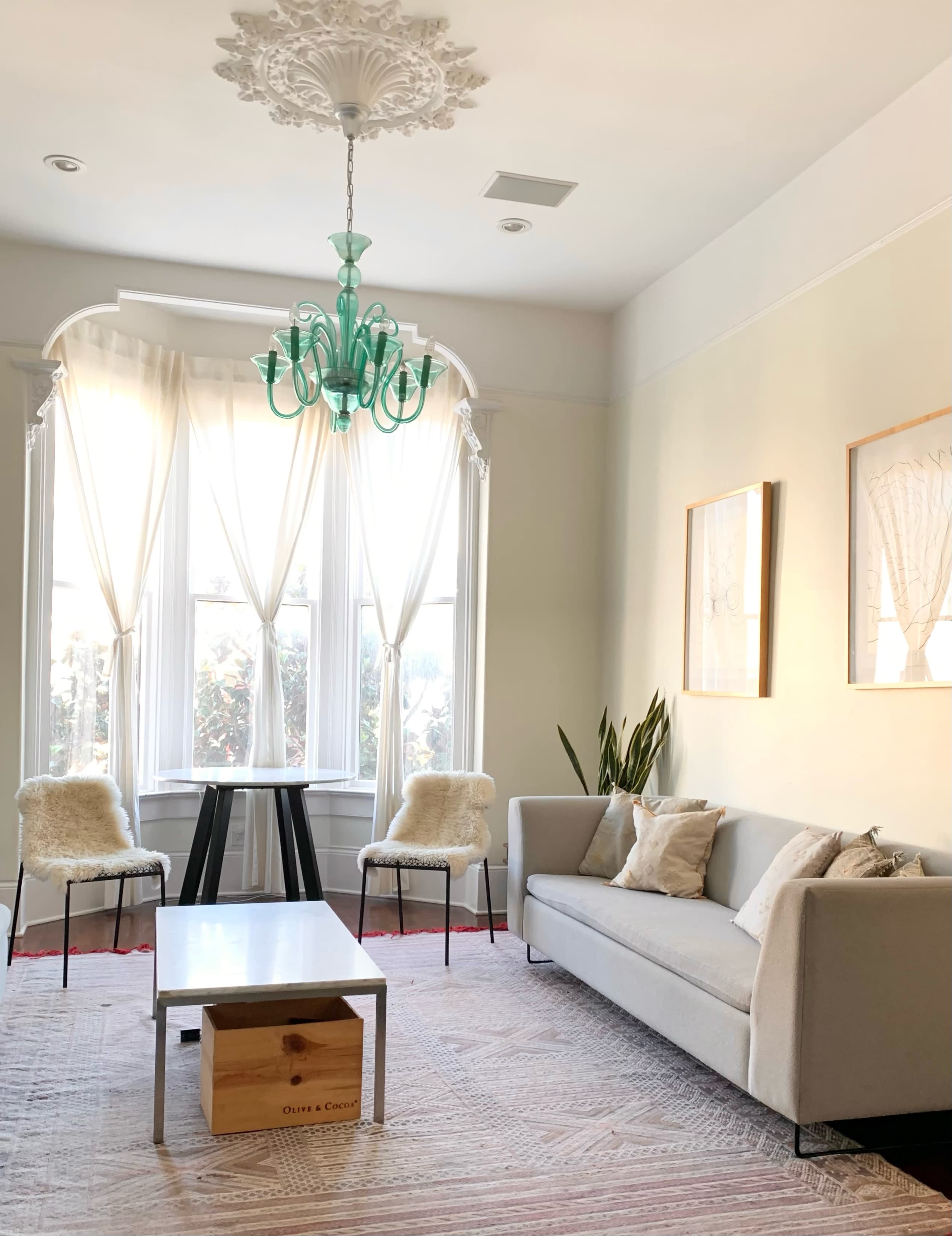 A bright living room with a gray sofa, two chairs, a coffee table, and large windows softly draped with sheer curtains.