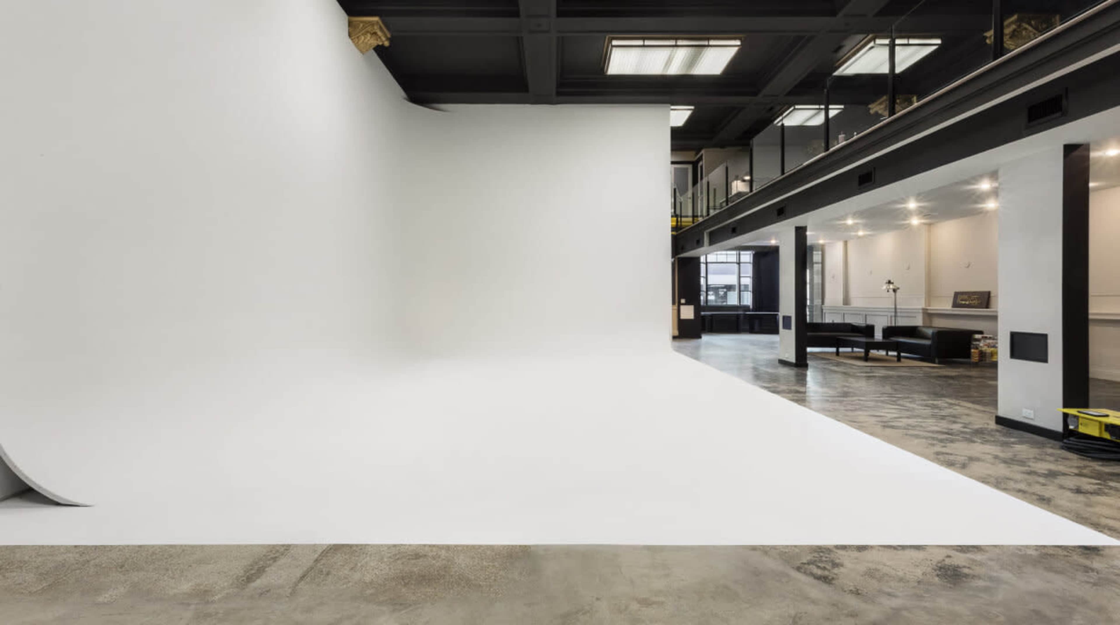 A spacious photography studio with a large white backdrop and polished concrete floors.
