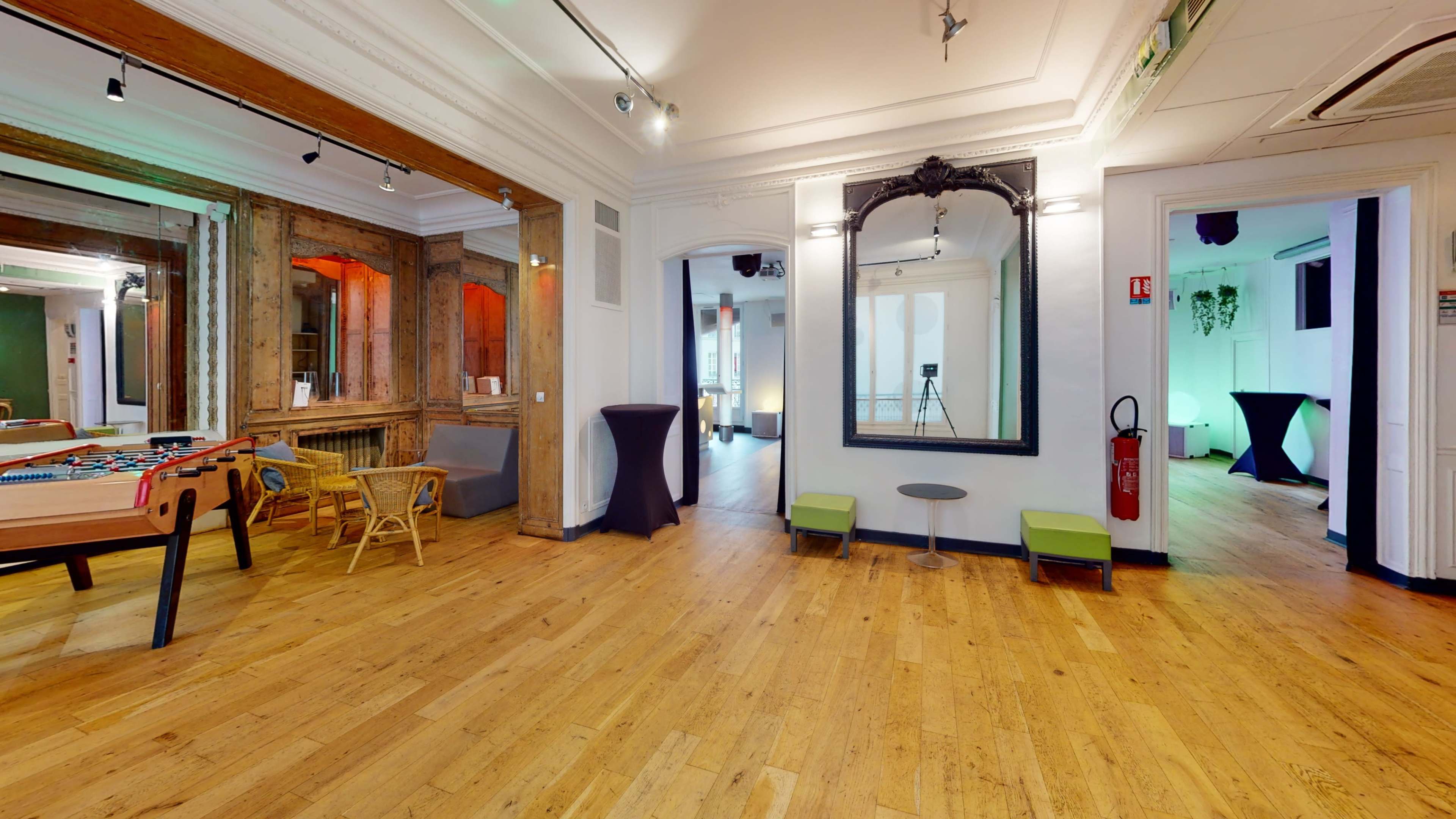 A spacious interior with wooden flooring, featuring a foosball table, chairs, and mirrors, along with two doorways leading to additional rooms.