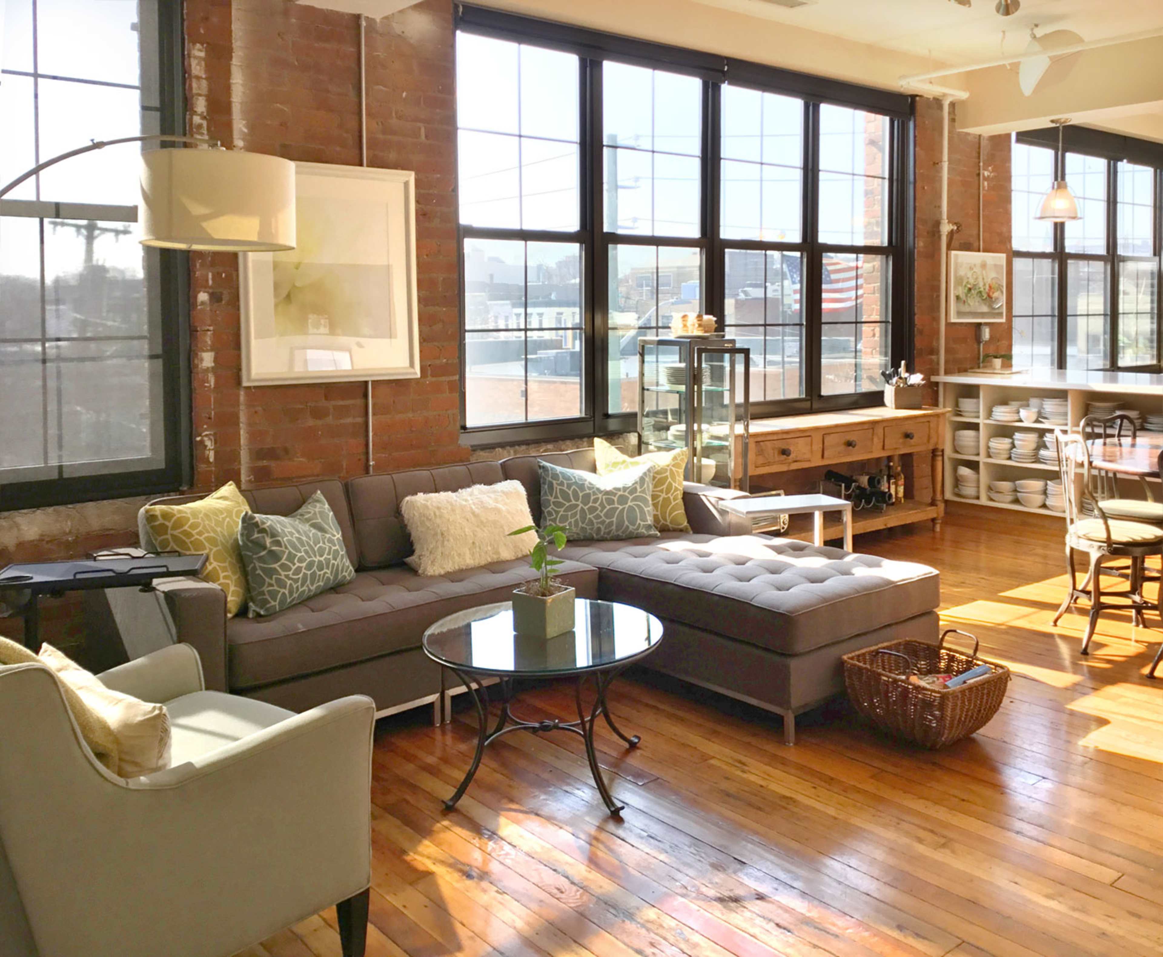 A spacious living area with large windows, a sectional sofa, a coffee table, and a dining space featuring wooden furniture.