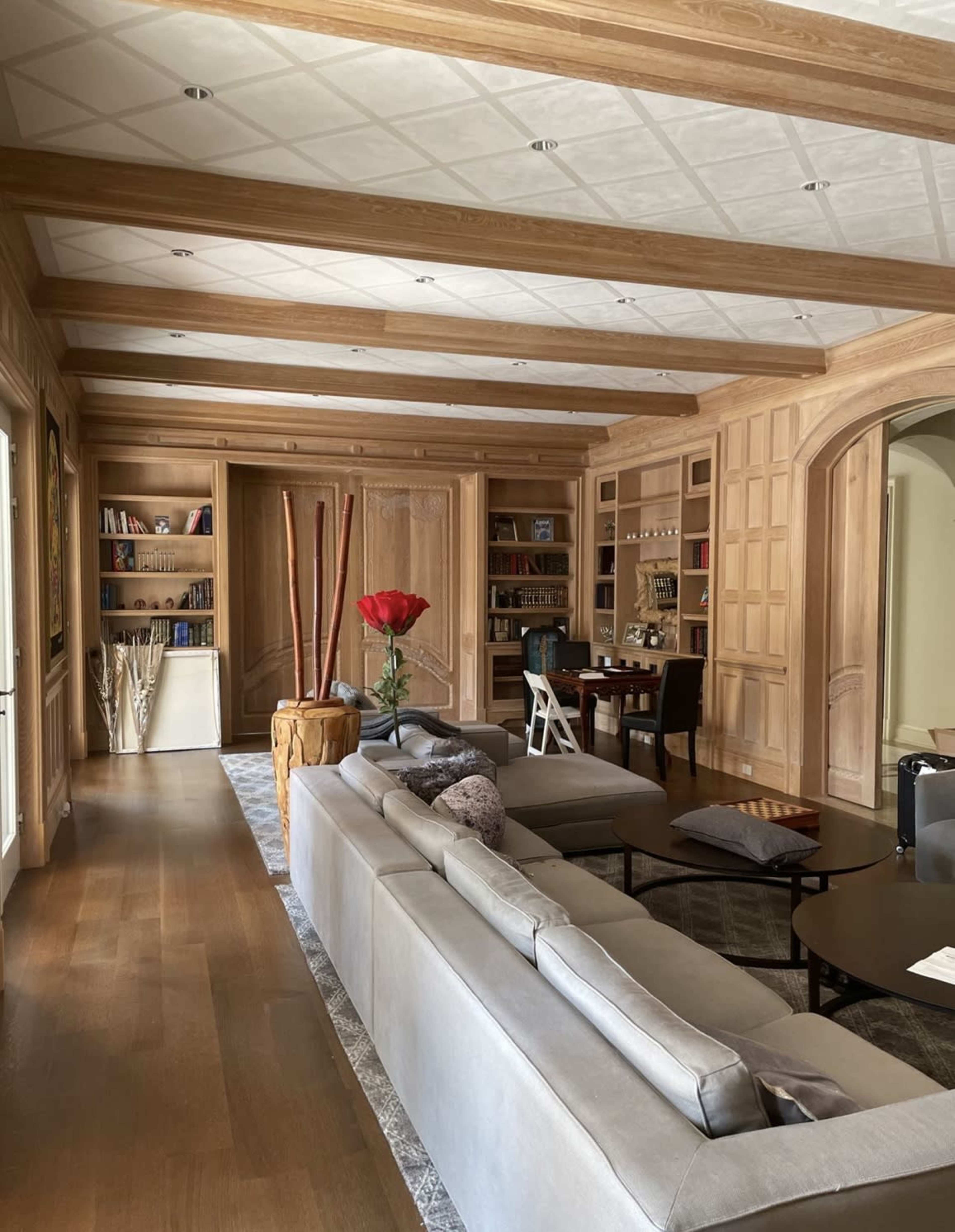 A spacious living room with wooden paneling, a large gray sectional sofa, and a coffee table, featuring a red flower arrangement as the focal point.